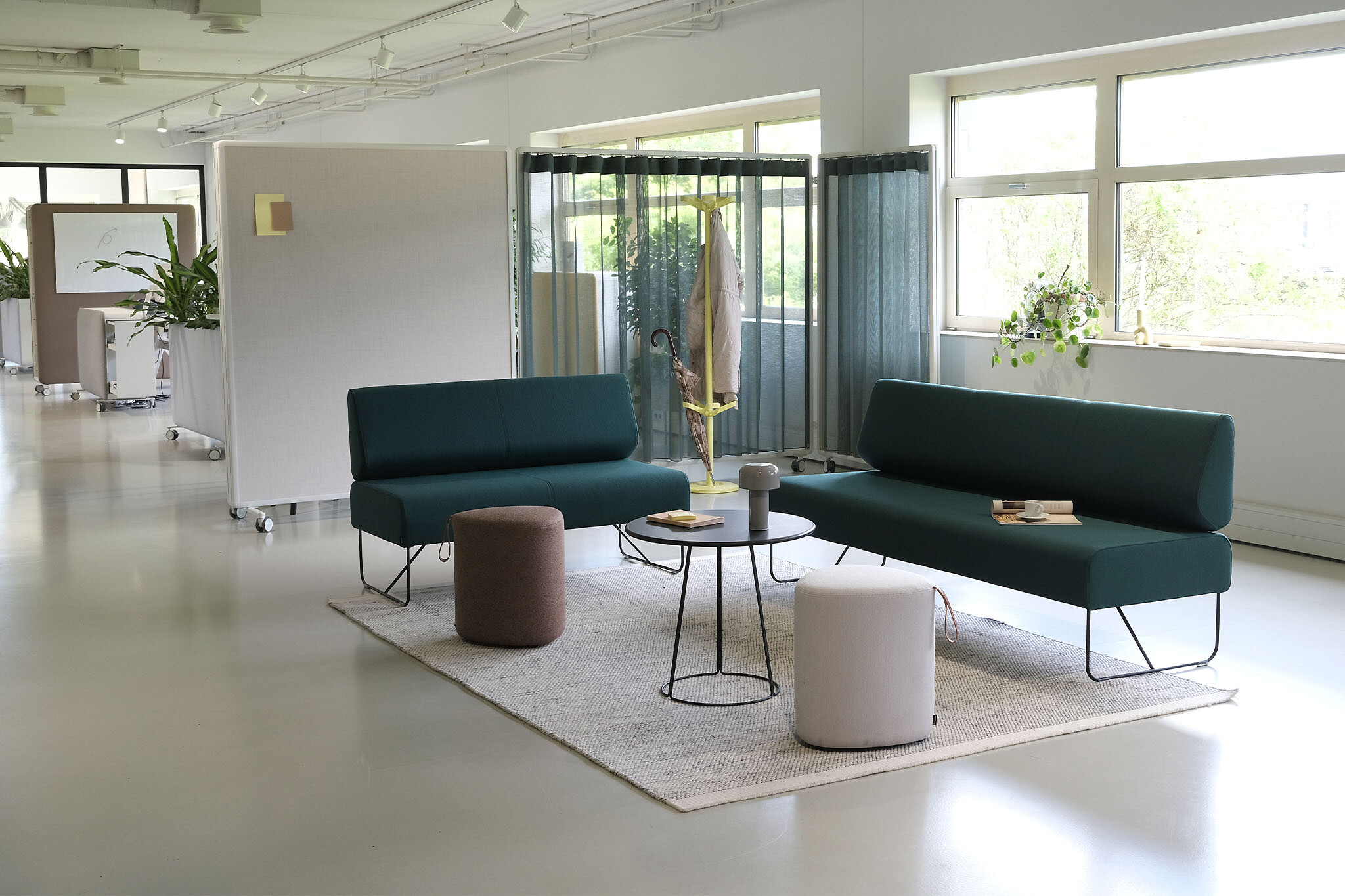Zwei grüne Sitzbänke mit Poufs, Couchtischen und Akustikpaneelen als Raumteiler