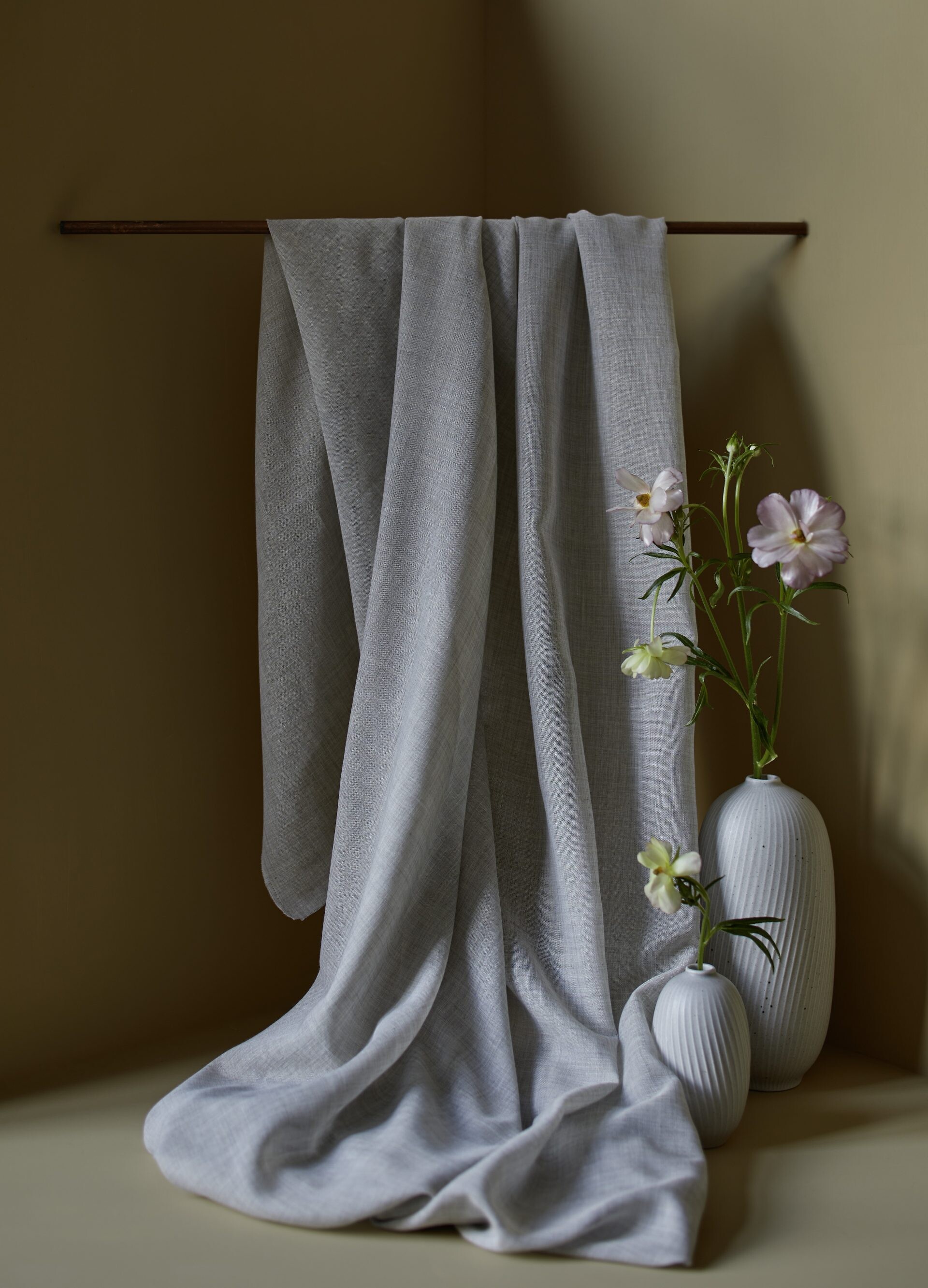 Graues Leinentuch über Stange mit Blumen in weißen Vasen im Vordergrund