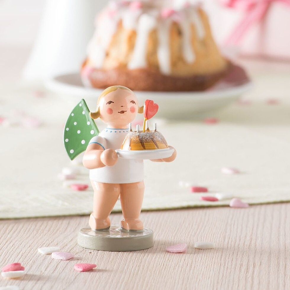 Engelfigur hält Gugelhupf mit Herz und Kerzendeko, dekoriert auf Kaffeetafel