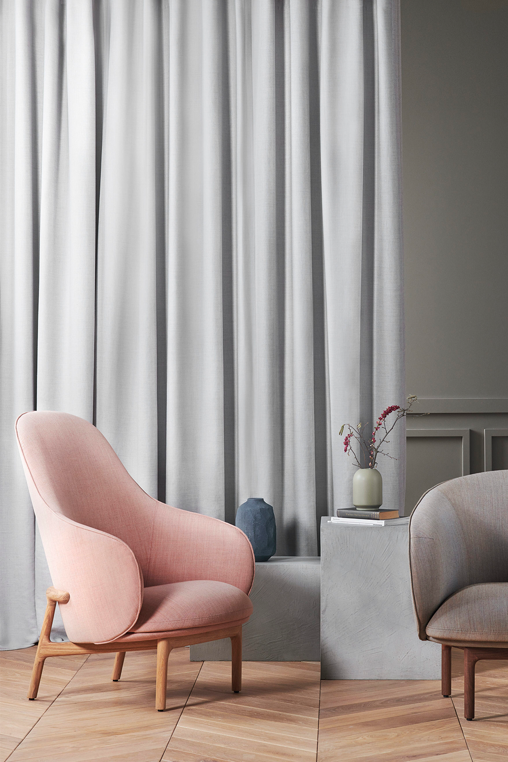 Zwei gepolsterte Lounge-Sessel aus Holzgestell vor einem hellgrauen Vorhang auf hellem Parkettboden.