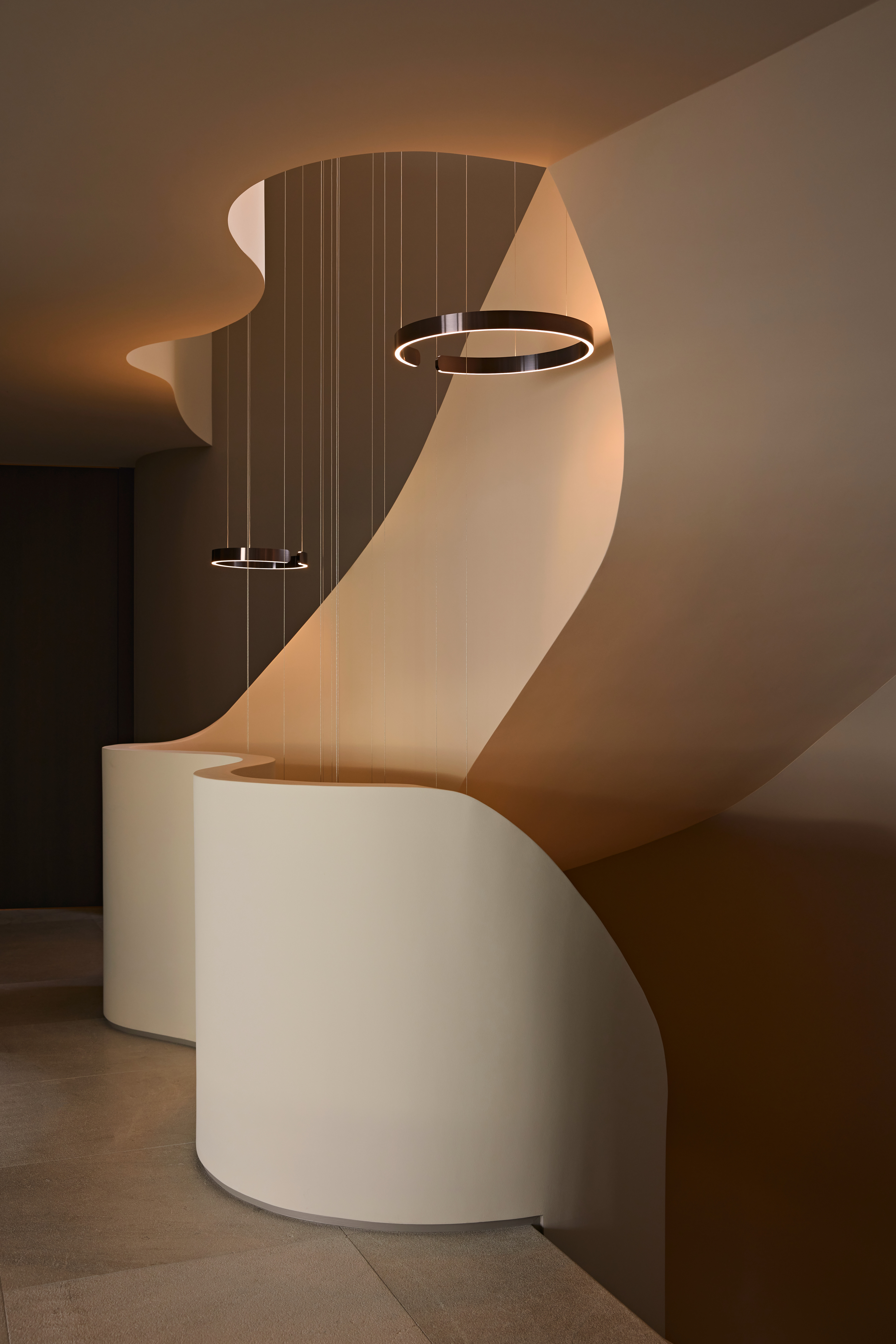Treppenaufgang mit organischer Wandform, beleuchtet durch zwei Occhio Mito sospeso Leuchten