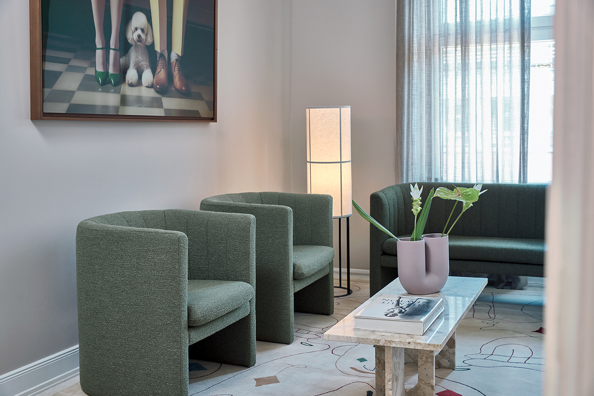 Ein geschmackvoll eingerichteter Wartebereich bei "Derma + Co." mit gemütlichen Loafer Sesseln und Sofa von &tradition, ergänzt durch den stilvollen Androgyne Coffee Table von Audo Copenhagen und die einzigartige Kink Vase von Muuto mit frischen Blumen.