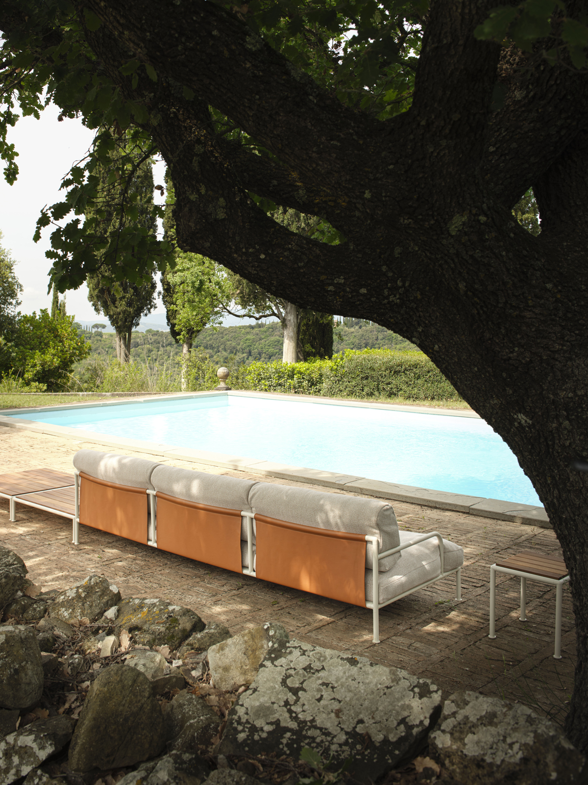 Outdoor-Sofa Roè von Fast mit hellen Polstern und Lederdetails am Pool, eingerahmt von Bäumen