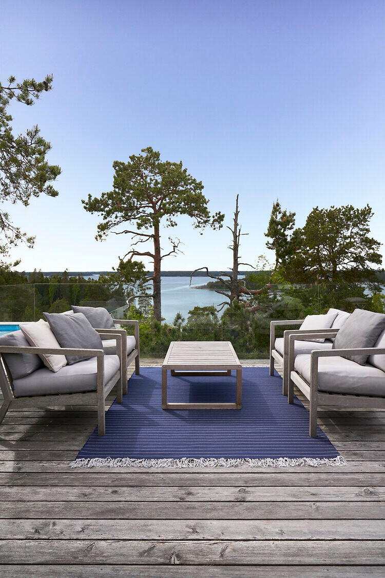 Terrasse mit blauen Outdoor-Teppichen, Lounge-Möbeln und Blick auf Wasserlandschaft