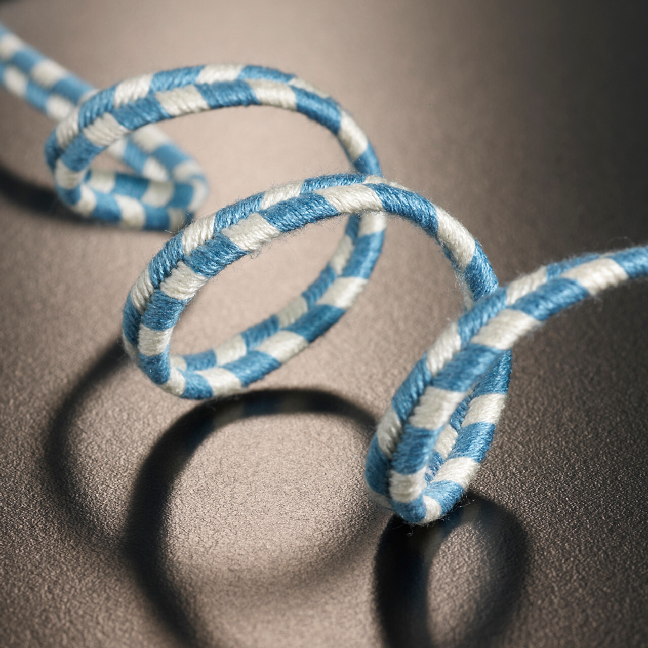 Blau-weiß gestreiftes Kordelband in dynamischer Spirale auf dunkler, leicht strukturierter Fläche