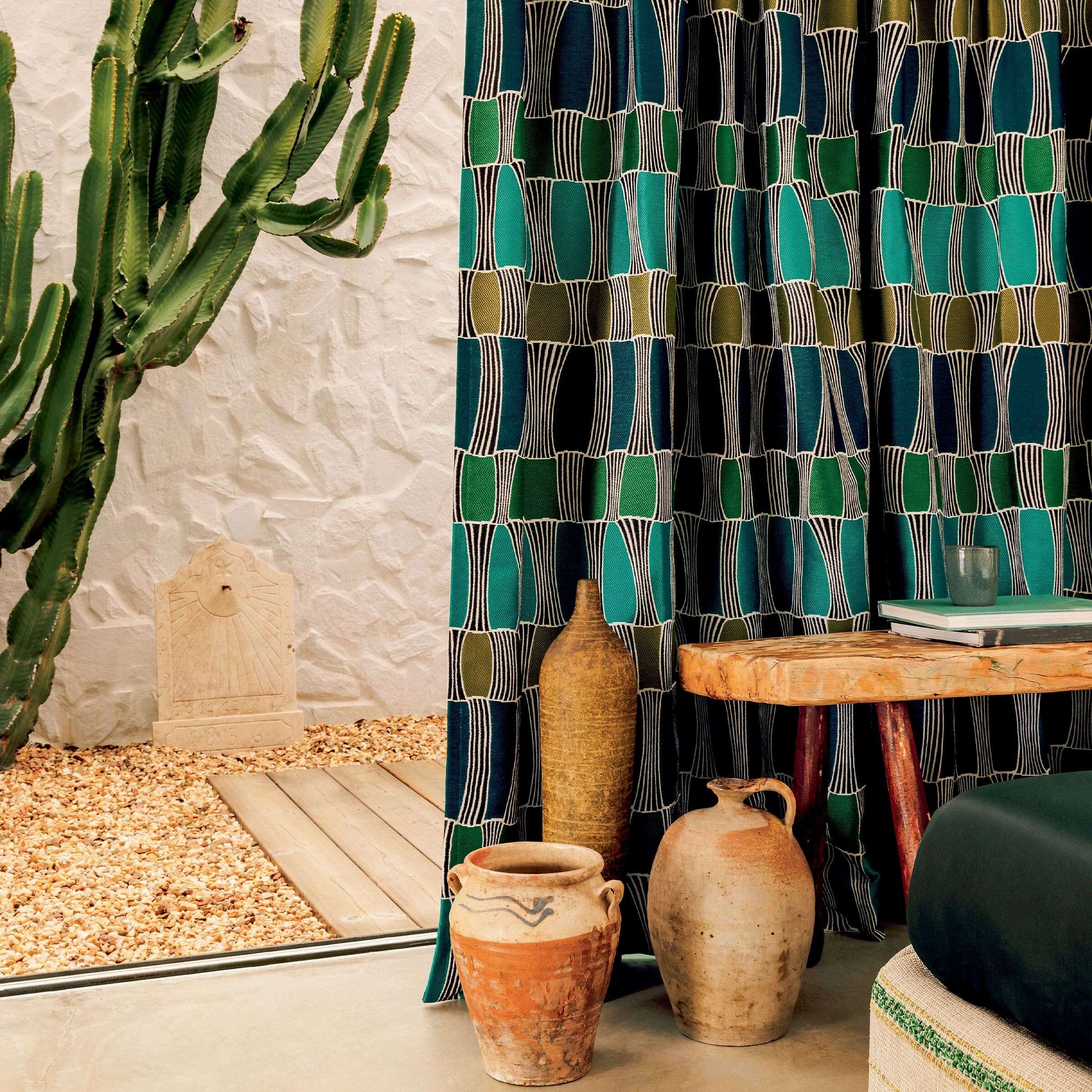 Vorhang mit grafischem Muster in Blau, Grün und Schwarz neben Tonkrügen und Kaktus am Fenster