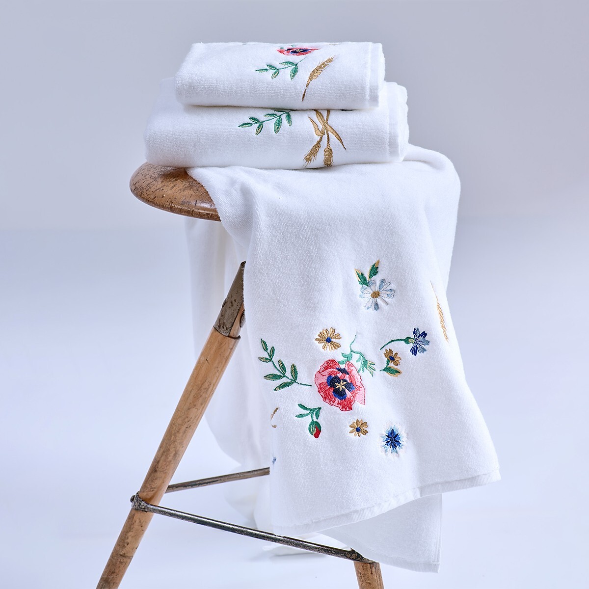Weißes Frottierhandtuch Set mit floraler Stickerei auf Holzhocker drapiert