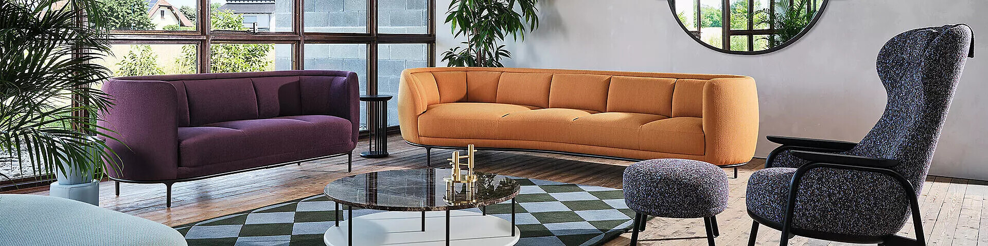 Zwei geschwungene Sofas in Orange und Violett, kombiniert mit Sessel und Couchtisch im WohnraumZwei geschwungene Sofas in Orange und Violett, kombiniert mit Sessel und Couchtisch im Wohnraum