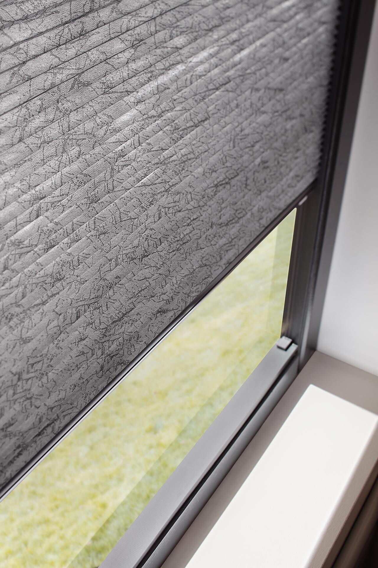 Fensterausschnitt mit strukturierter, grauer Plisseeanlage in Wabenoptik