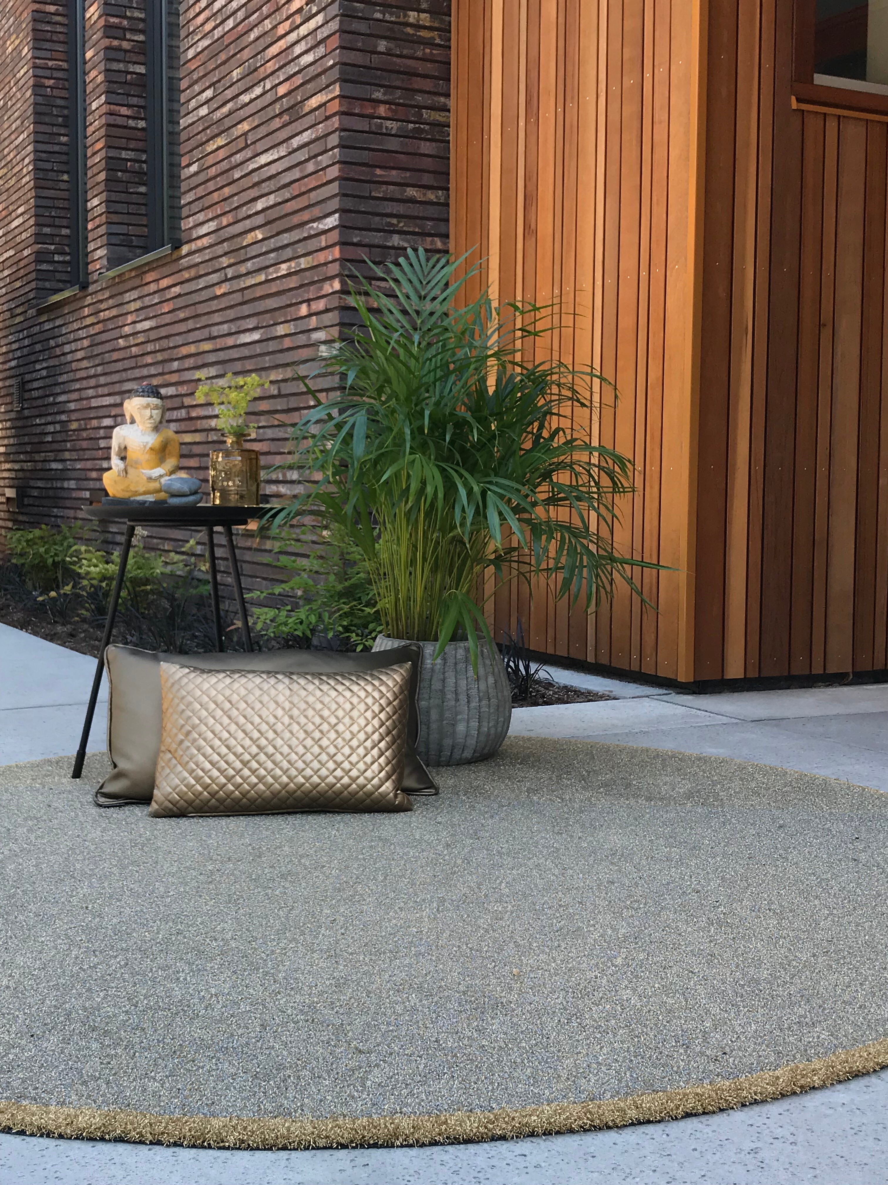 Runder Teppich auf einer Terrasse vor Fassade aus Holz und Backstein, dazu Deko
