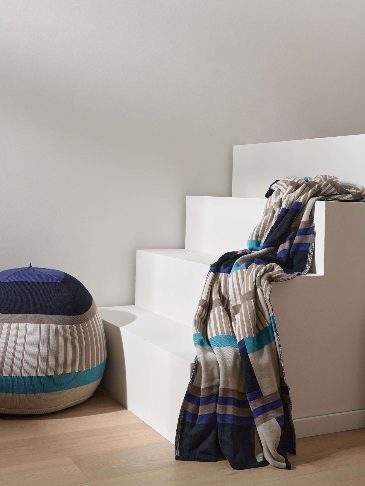 Gestrickter Pouf in Blau mit passender Decke auf weißer Treppe arrangiert