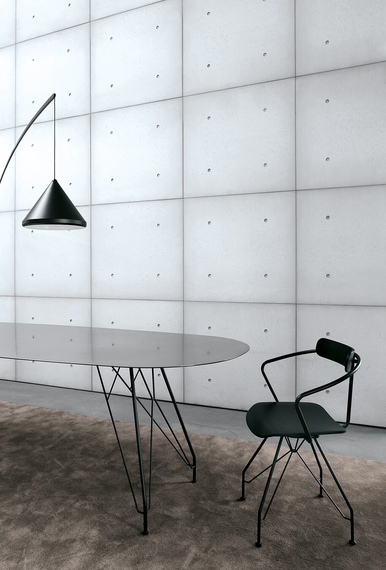 Schwarzer Designerstuhl mit Armlehne an einem ovalen Glastisch vor einer hellgrauen Betonwand