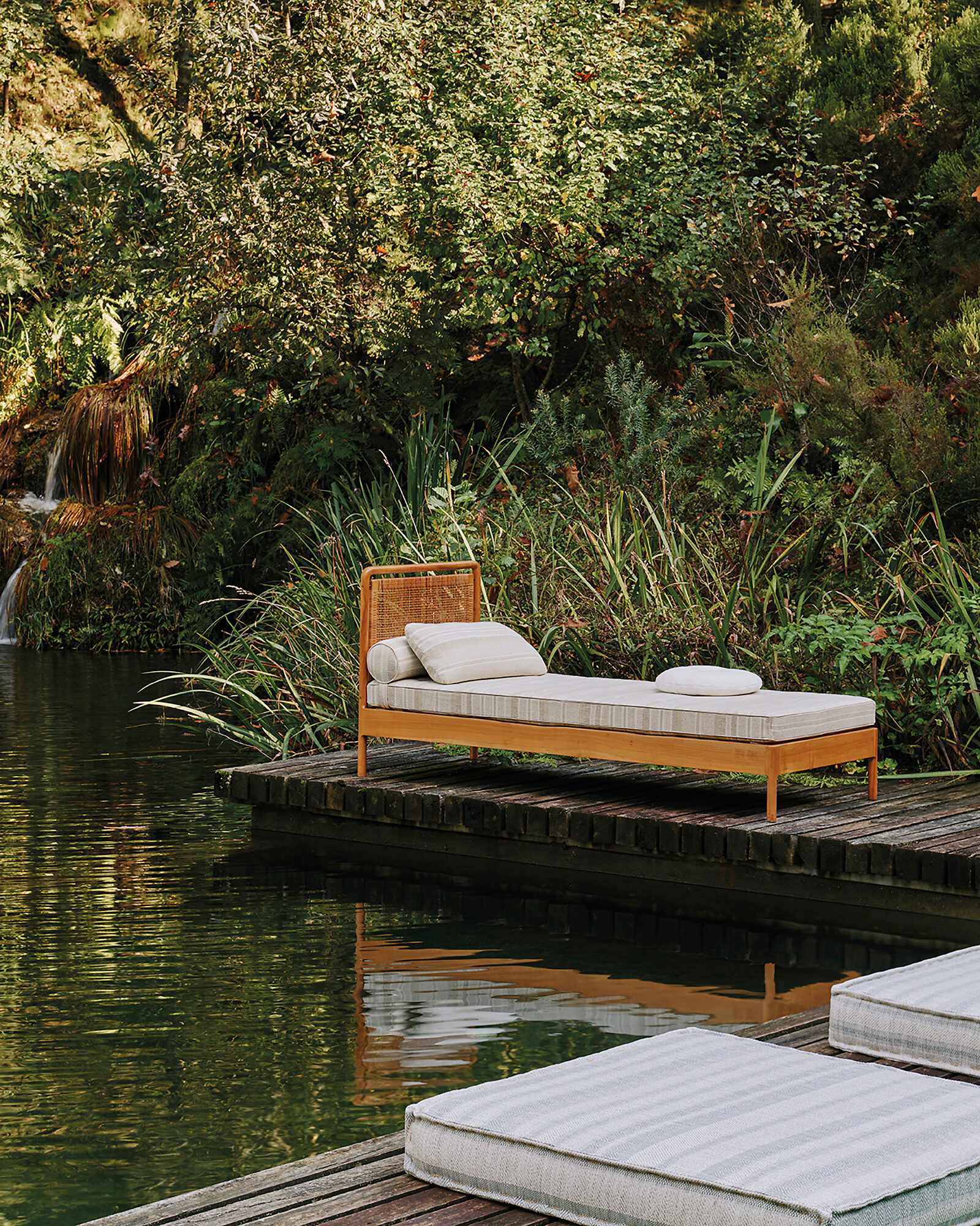 Outdoor-Liege mit hellem Polsterbezug auf Holzsteg vor grünem Hintergrund