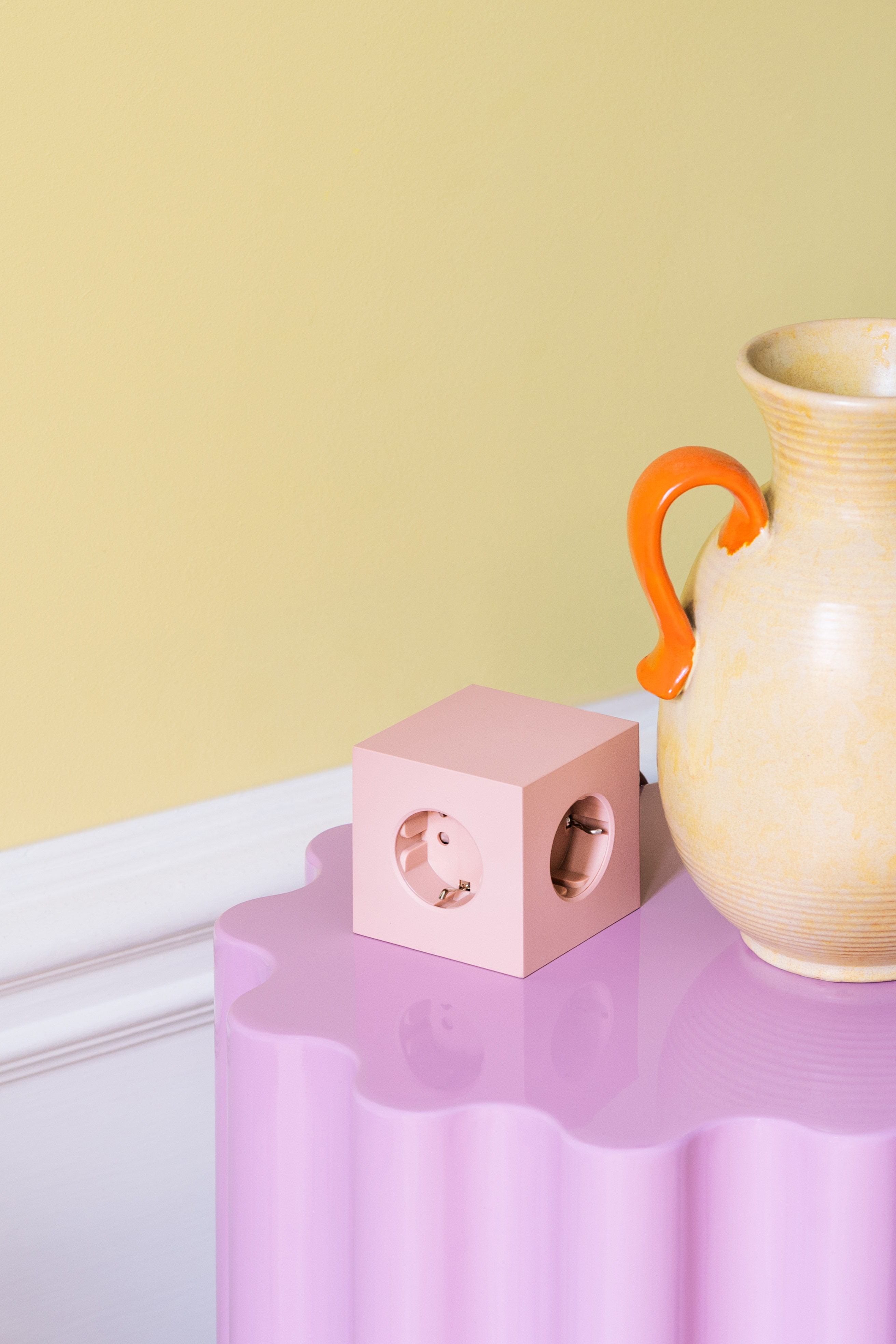 Der Extender Square von Avolt in Rosa auf einem lilafarbenen Tisch, daneben eine Keramikvase