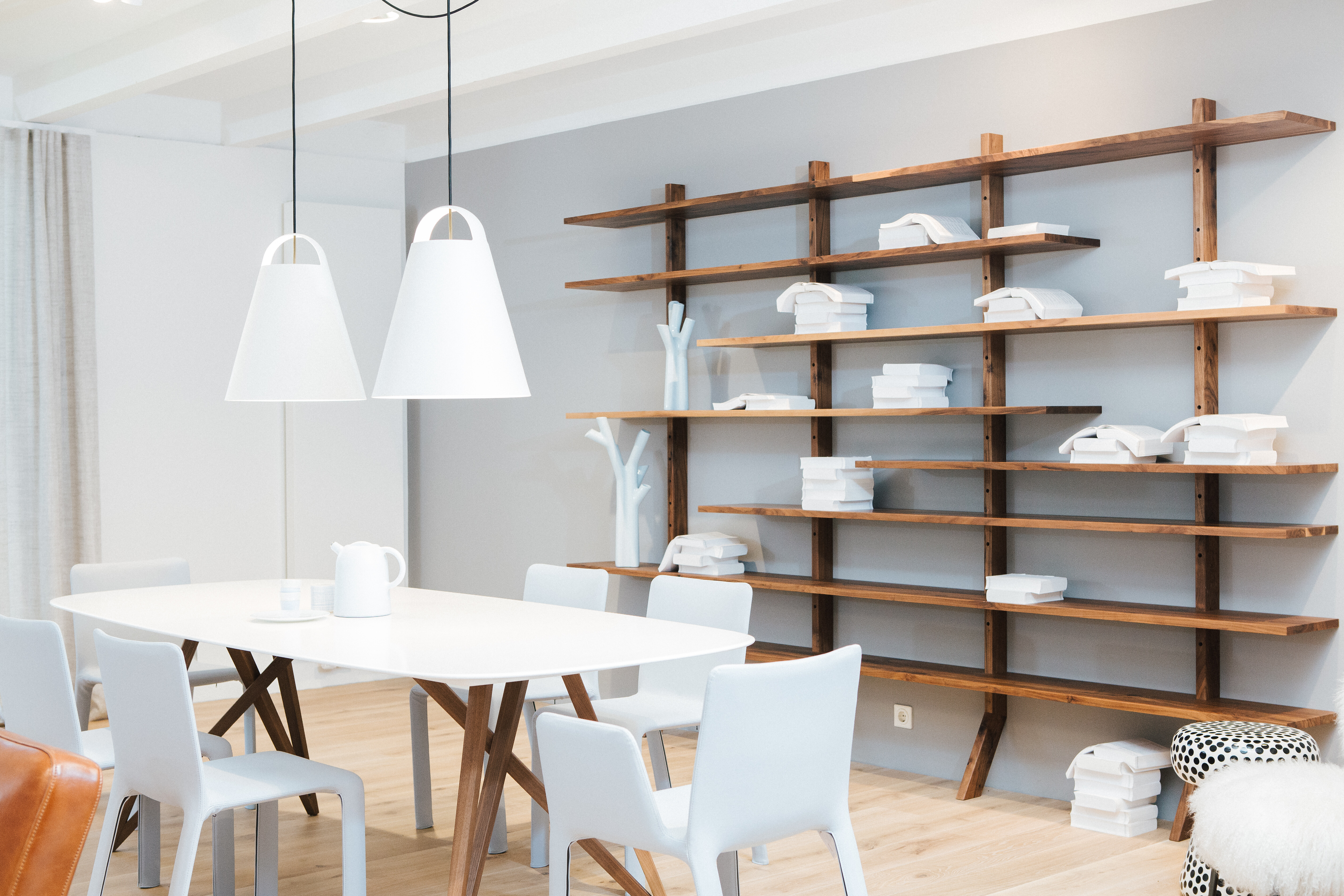 Essbereich mit weißem Tisch, hellen Stühlen und großem Wandregal aus Holz in ruhiger Umgebung