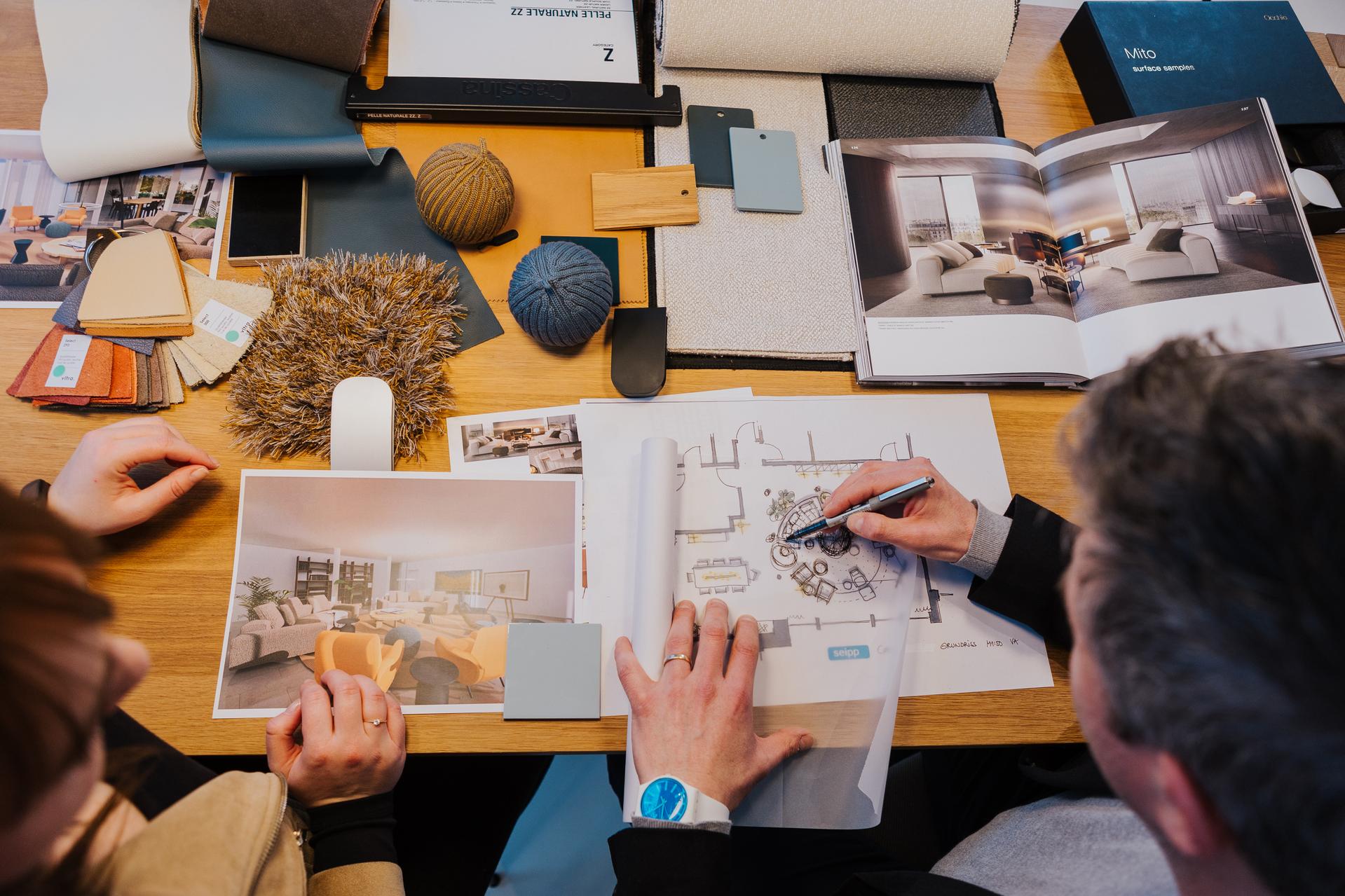 Innenarchitektonisches Planungsgespräch mit Grundriss, Mustern und Visualisierungen auf dem Tisch.