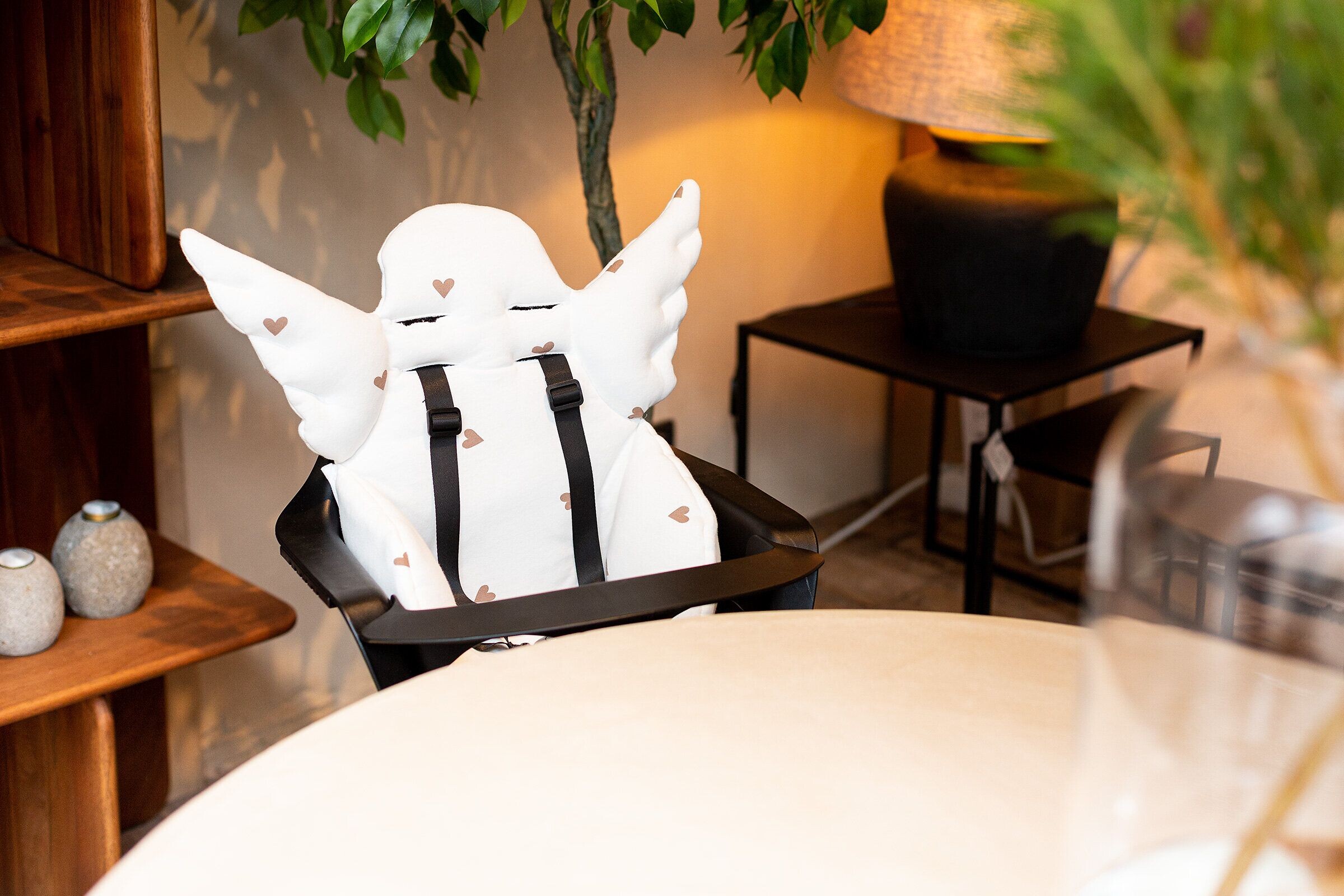 Kindersitz mit Flügelkissen an einer Esszimmerstuhllehne vor grünem Blätterhintergrund