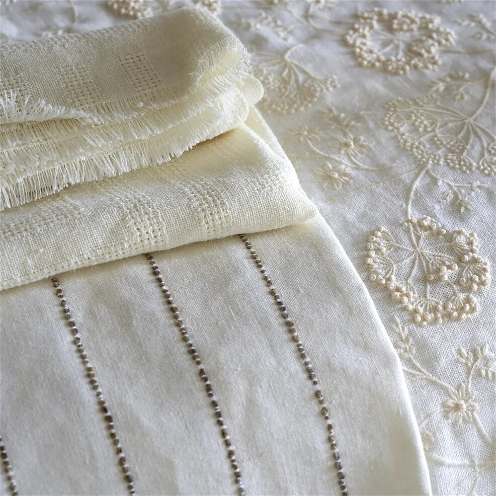 Gestapelte Stoffe in Cremeweiß mit zarten Stickereien und eingewebten Strukturen
