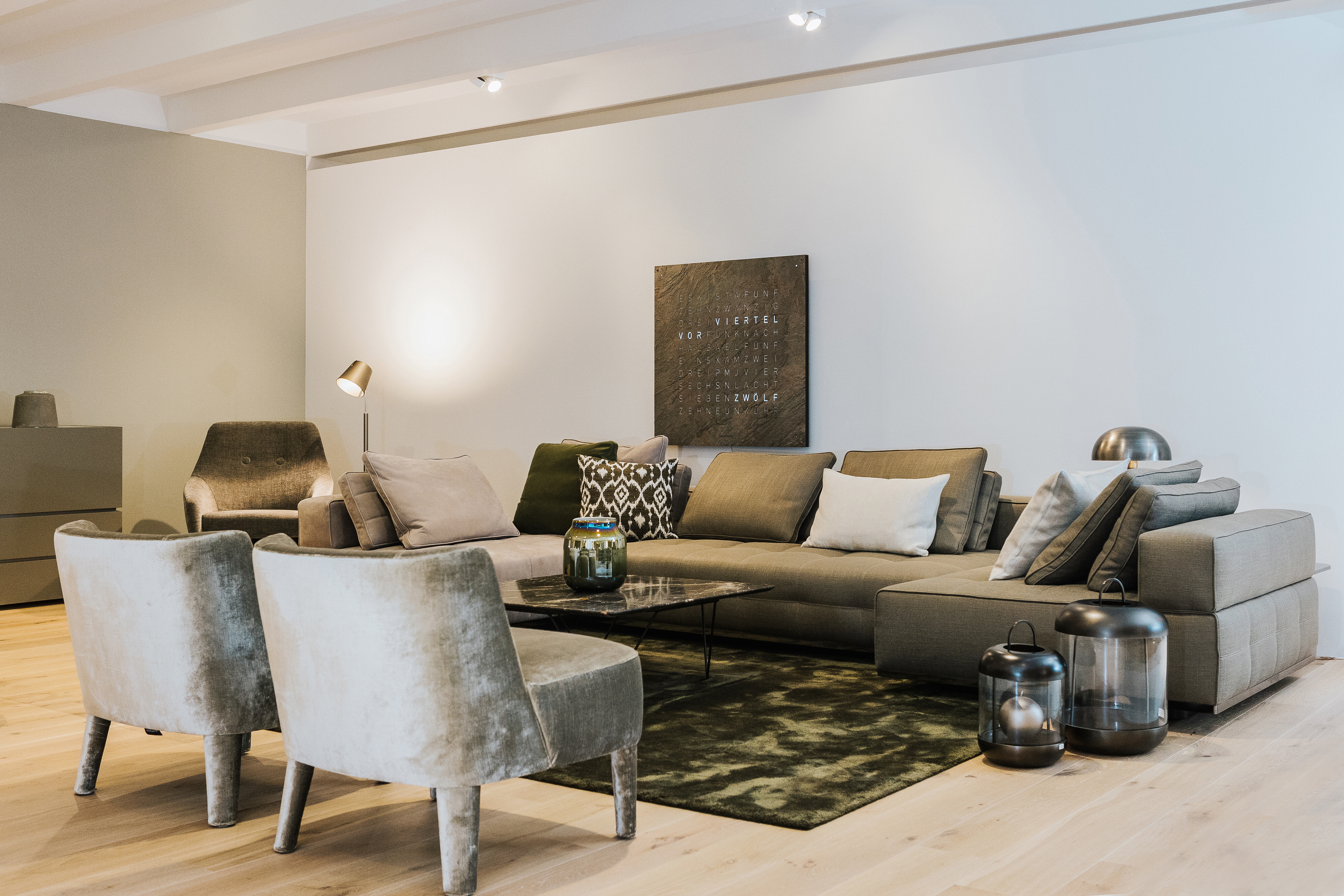 Wohnraum mit großer Sofalandschaft in Taupe, zwei Sesseln und Qlocktwo Wanduhr über dem Sofa