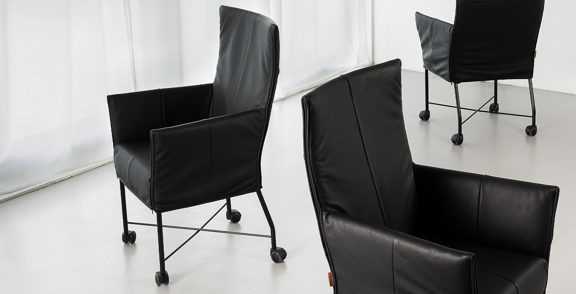 Zwei schwarze Ledersessel auf Rollen, auf hellem Boden vor weißem Hintergrund