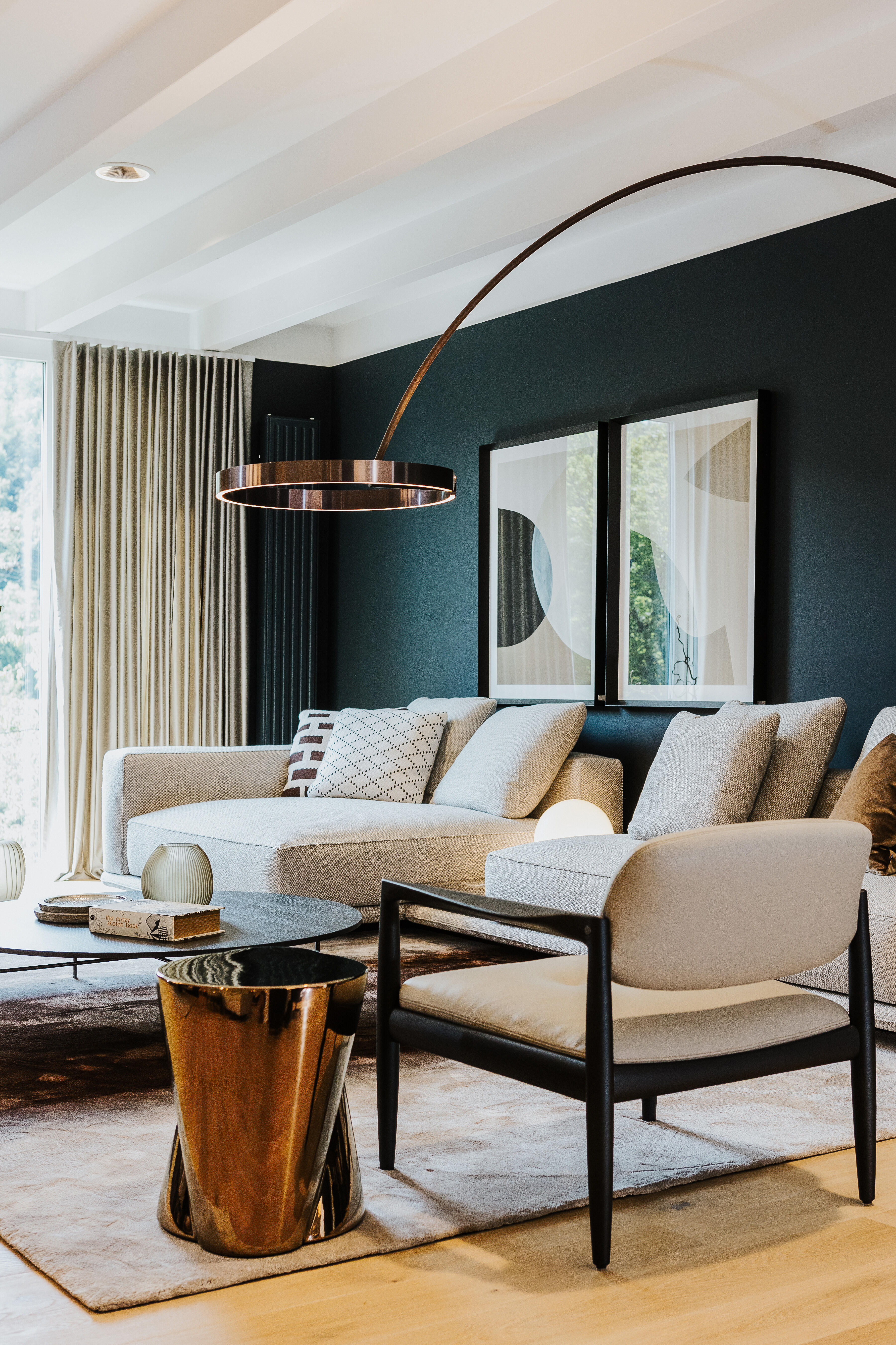 Eleganter Wohnbereich mit hellem Sofa, schwarzem Sessel, Occhioleuchte und goldfarbenem Beistelltisch