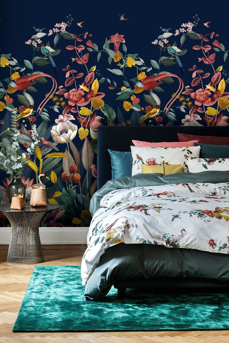 Dunkle Wandtapete mit farbenfrohem Blumenmuster hinter einem Bett mit floraler Bettwäsche