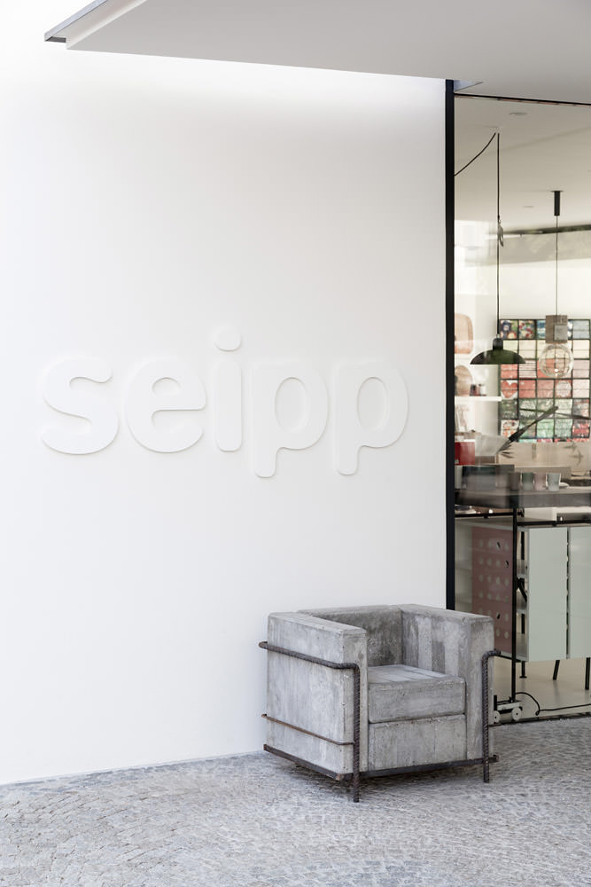 Eingang von Seipp Wohnen Waldshut mit weißer Fassade, eingelassenem Logo und Beton-LC2 von Stefan Zwicky. Durchblick in den Showroom im Hintergrund.