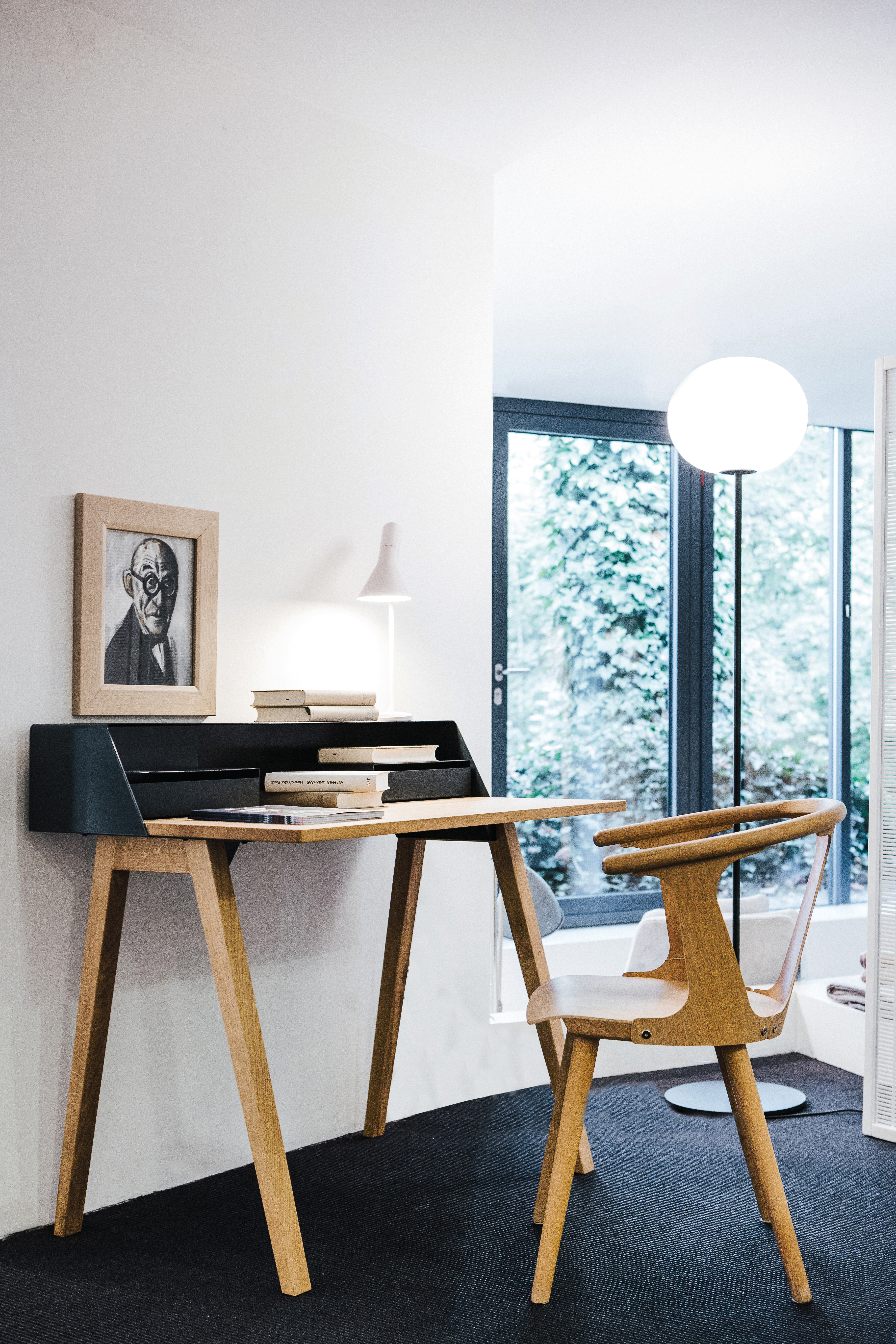 Kompakter Schreibtisch mit Holzgestell und passendem Stuhl in heller Ecke mit Stehleuchte im Hintergrund