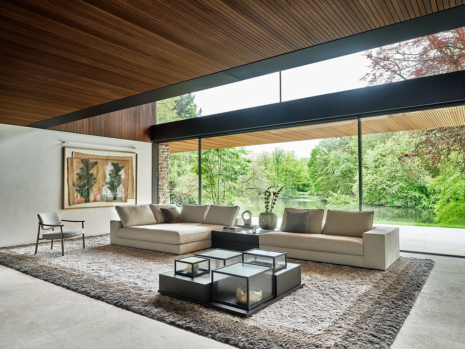 Großzügiges Sofa mit Glas-Couchtischen auf Hochflorteppich vor Panoramafenster