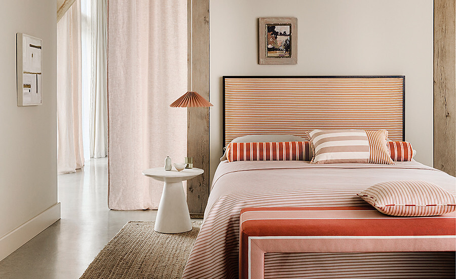 Gestreifter Stoffbezug in Orange und Rosé auf Bett und Kissen in heller Umgebung