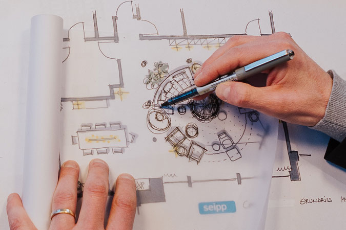 Hand zeichnet mit Stift an architektonischer Skizze auf Planunterlage