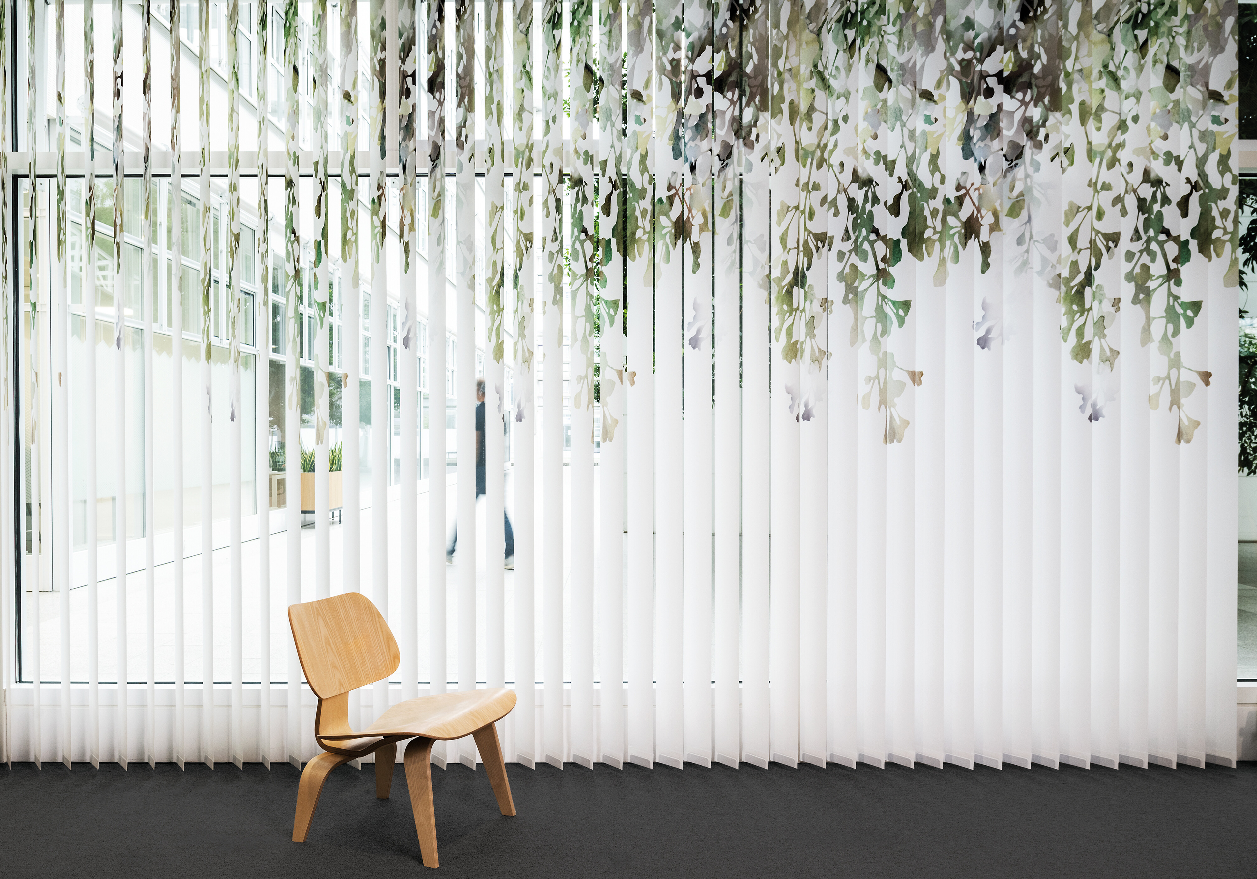 Weiße Vertikallamellen mit floraler Bedruckung vor verglastem Raum und Holzstuhl
