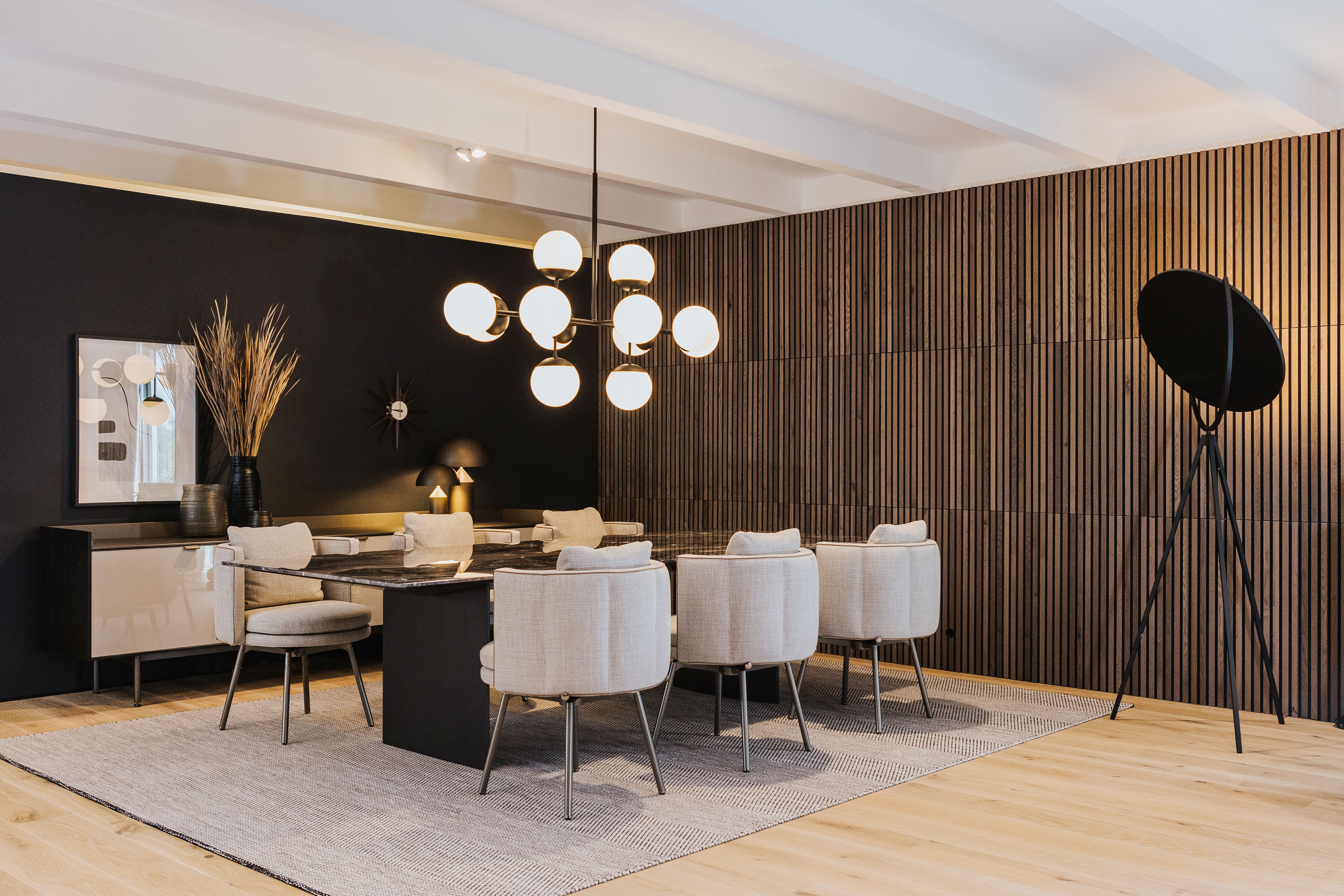 Essbereich mit gepolsterten Stühlen und der Hängeleuchte Lord Ballroom von RUBN vor Holzlamellenwand