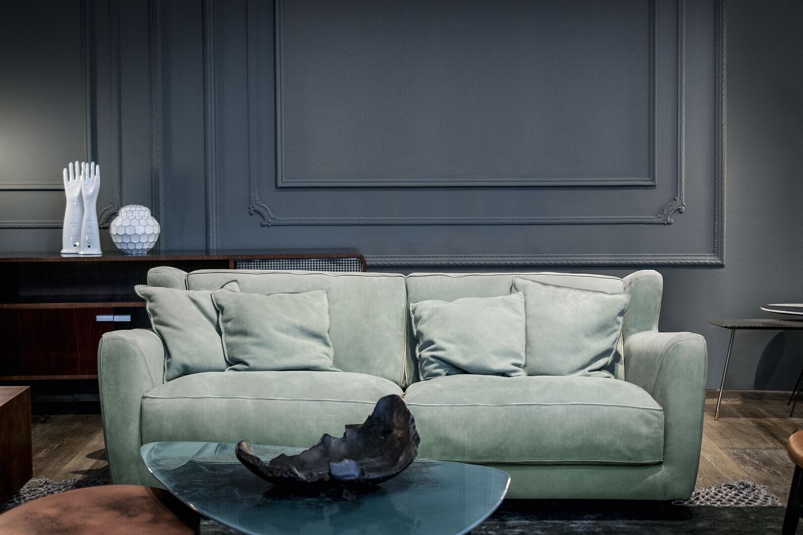 Sofa in hellem Mintgrün mit vier Kissen vor dunkelgrauer Wandvertäfelung