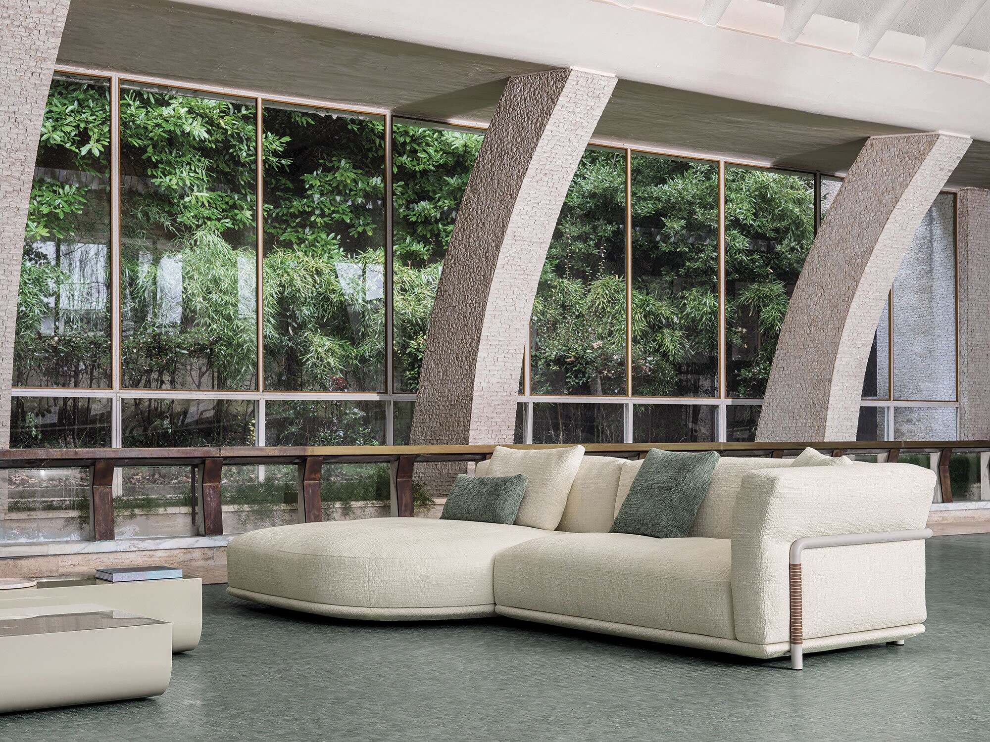 Hellbeiges Sofa mit Recamiere vor hohen Fenstern und begrüntem Außenbereich