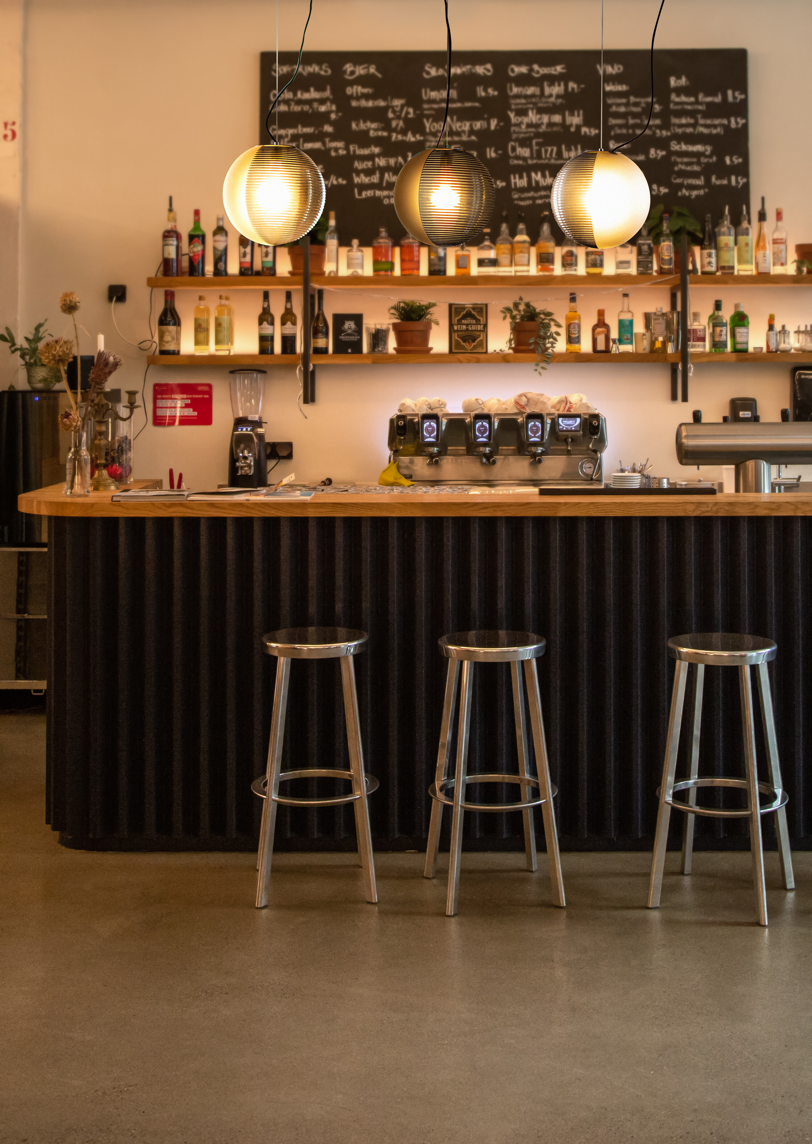 Drei Pendelleuchten über Bartheke mit Hockern, Regal und Kreidetafel im Hintergrund