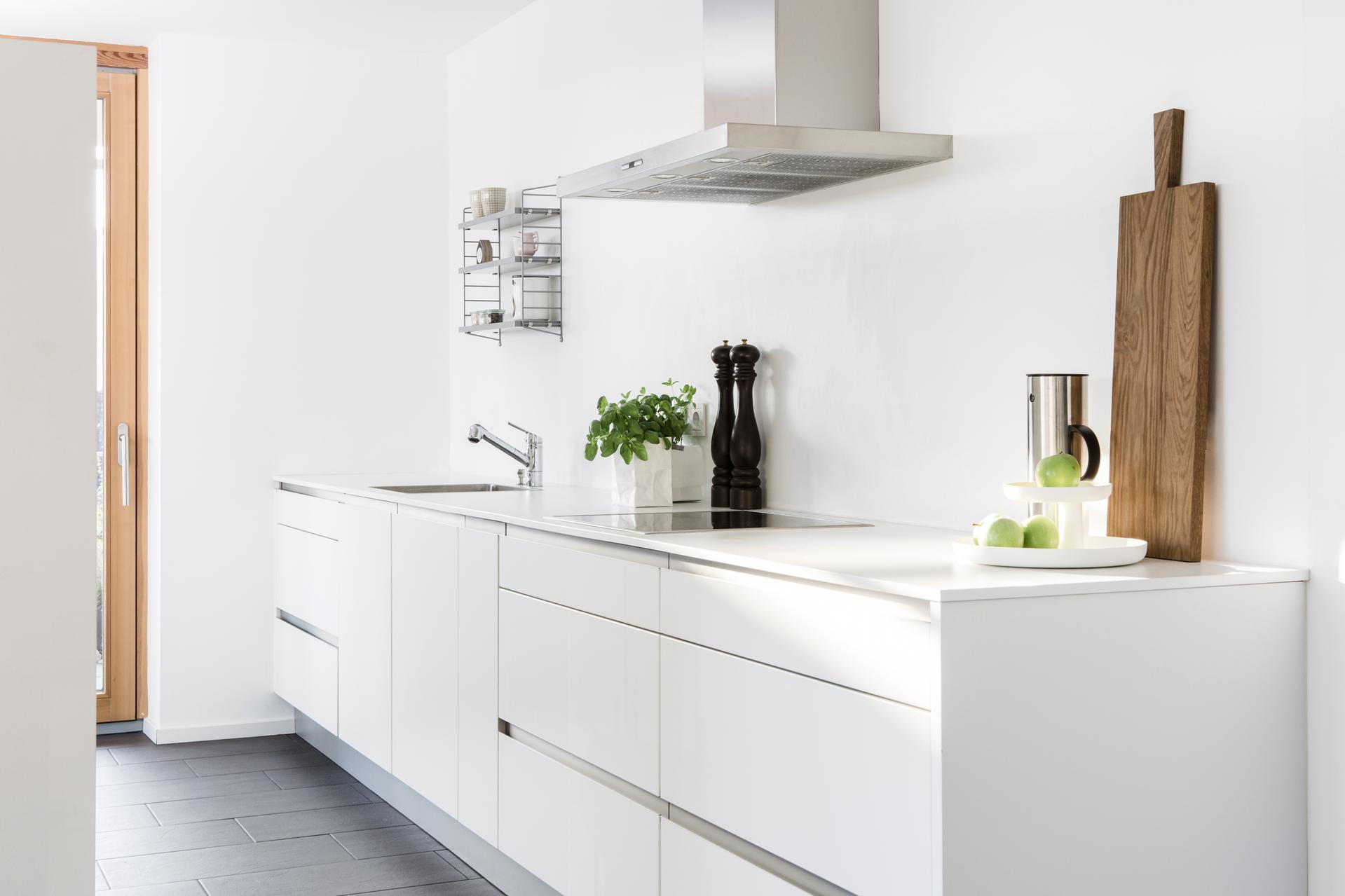 Die klare Küche von Nolte wurde komplett in weiß gehalten. Eine Besonderheit ist der freistehende Block inklusive Backofen, Kühlschrank und jede Menge Stauraum, welcher gleichzeitig als Raumteiler zwischen Koch- und Essbereich fungiert. Die breiten Griffm