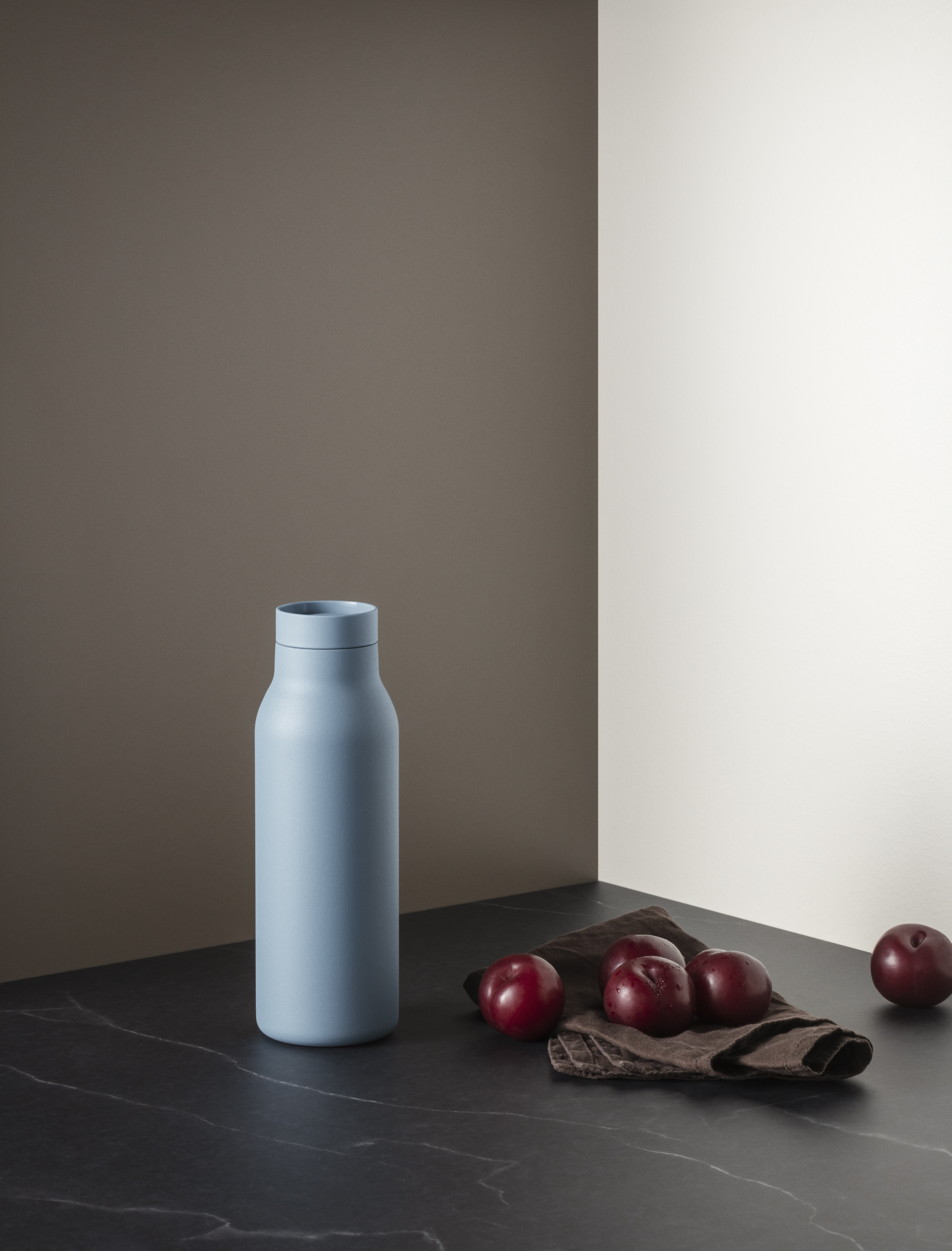 Urban Thermosflasche in Dusty Blue von Eva Solo vor minimalistischer Kulisse mit Pflaumen