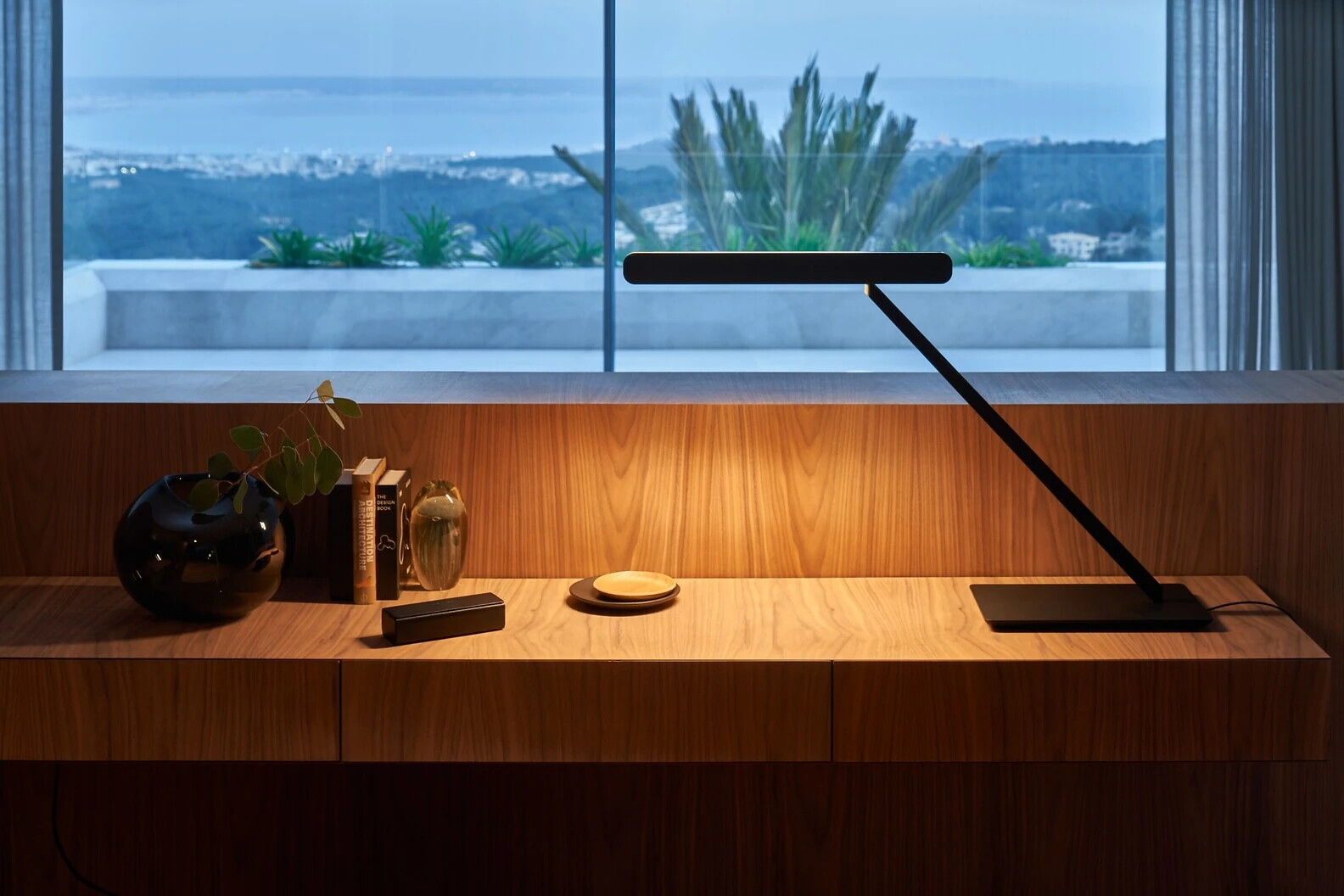 Schreibtischleuchte Taglio tavolo von Occhio auf Holzkonsole vor Fenster mit Ausblick