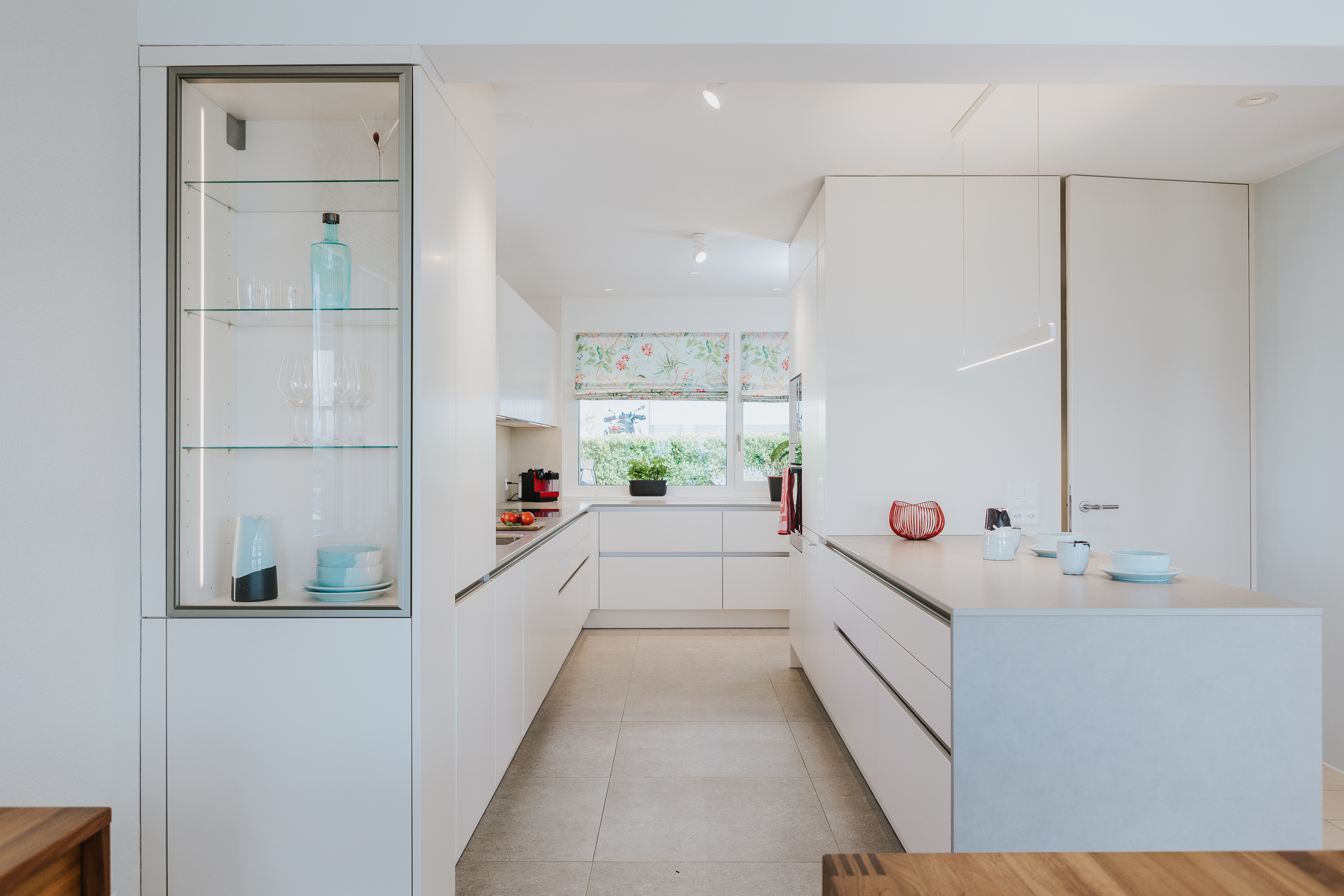 Küche mit weißen Fronten, klarer Linienführung und hellgrauer Kochinsel in lichtdurchflutetem Ambiente.