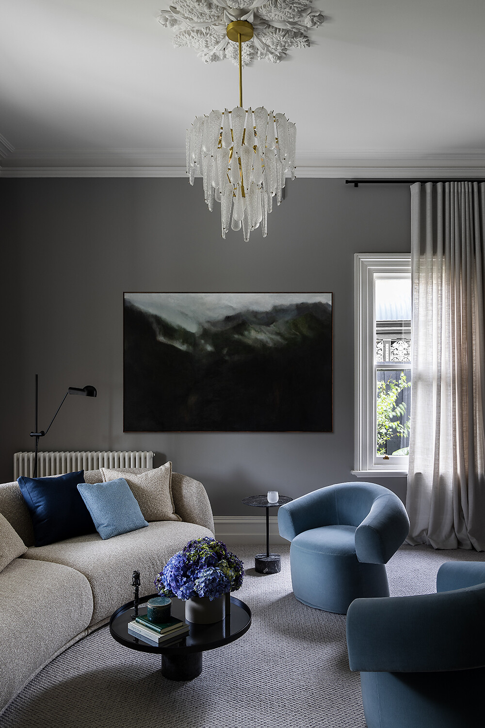 Wohnbereich mit weichem Sofa, blauen Sesseln und dunklem Gemälde an der Wand