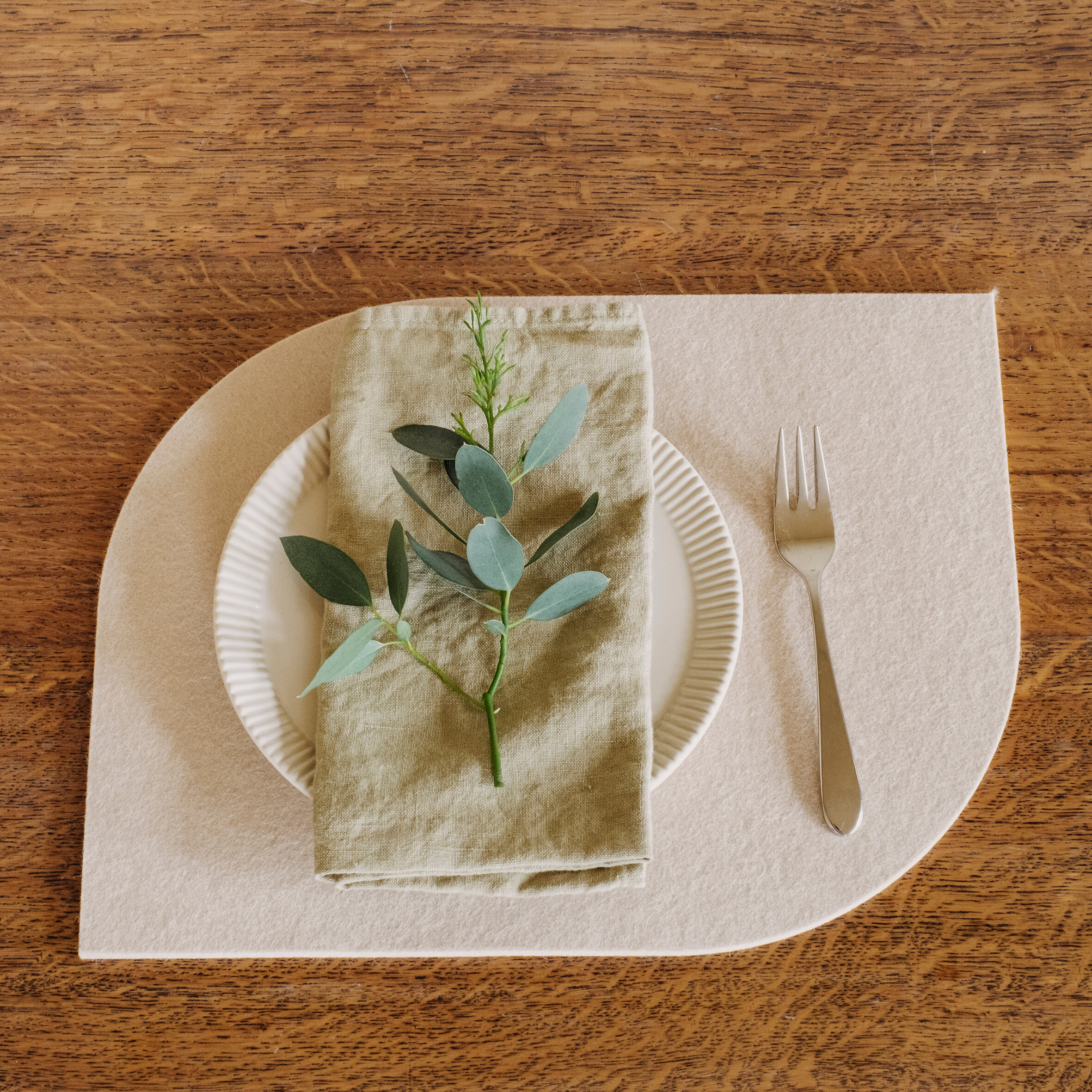 Tischset in Cremeweiß unter Teller mit Stoffserviette und Eukalyptusdeko auf Holztisch