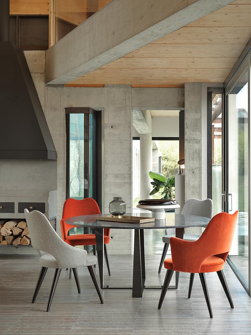 Esstisch aus Glas mit gepolsterten Stühlen in Orange und Beige im Betonraum