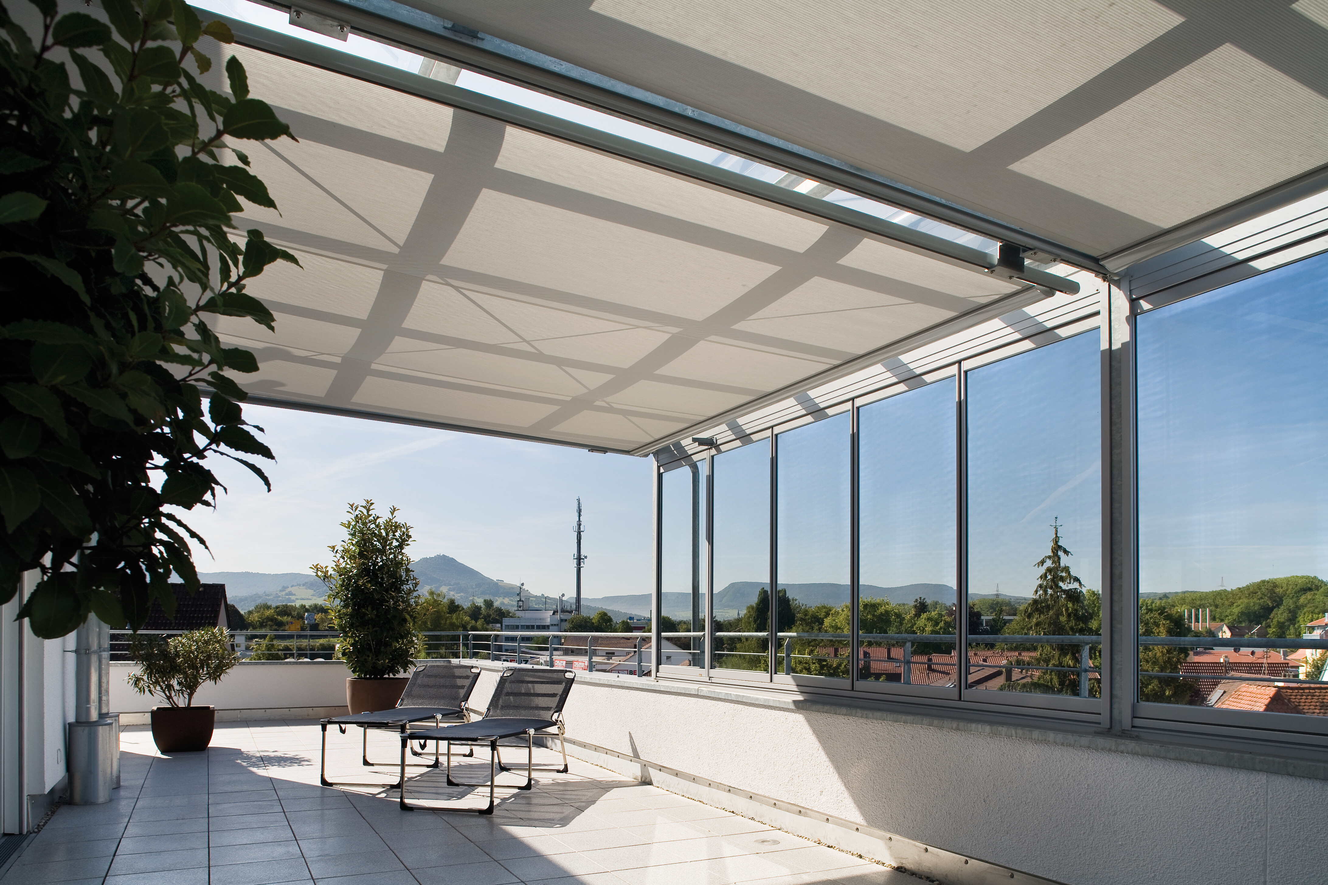 Terrasse mit großer Markise unter Glasdach, zwei Sonnenliegen