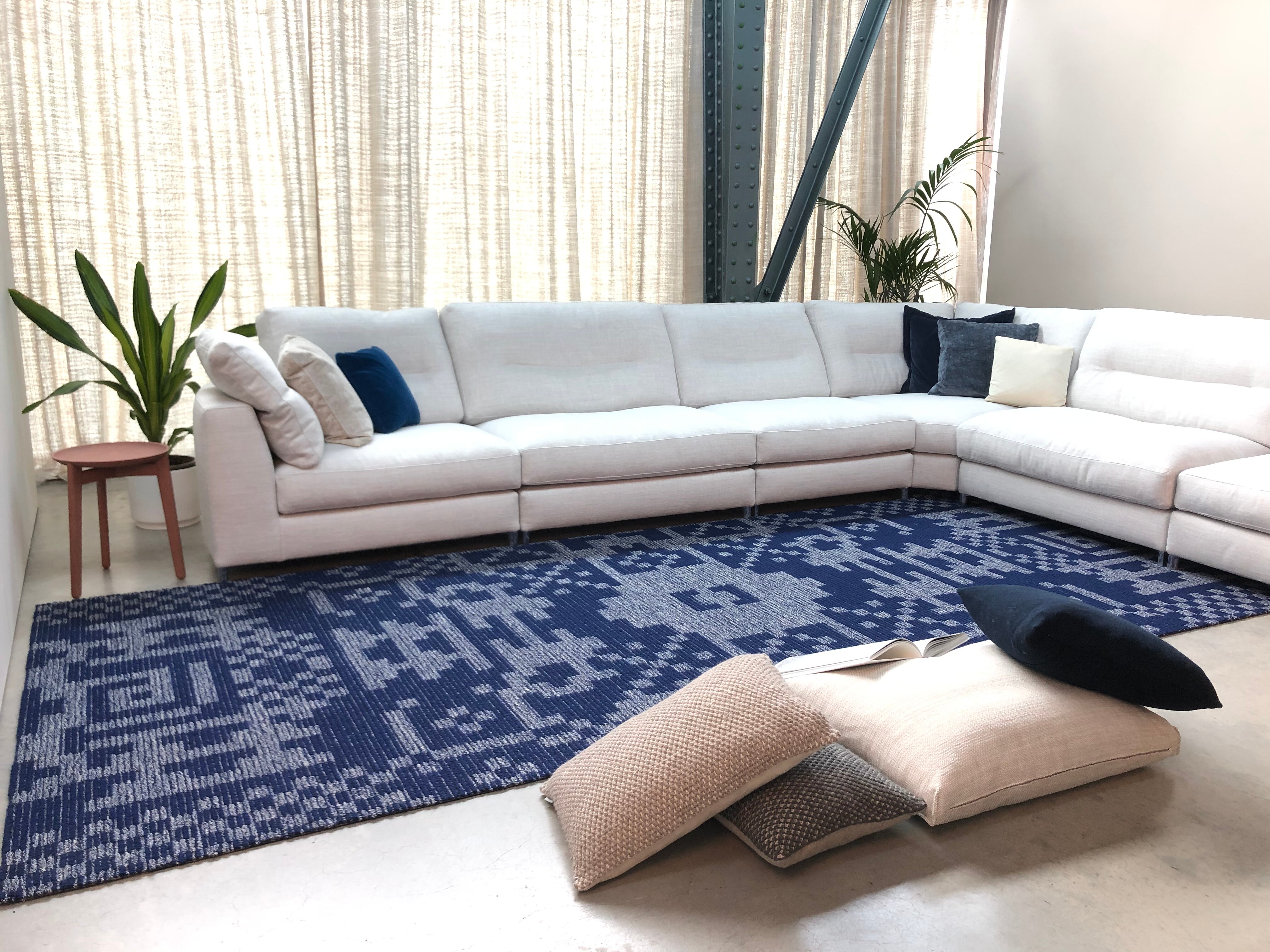 Großer Teppich mit blauem Muster vor einem weißen Ecksofa in einem lichtdurchfluteten Raum