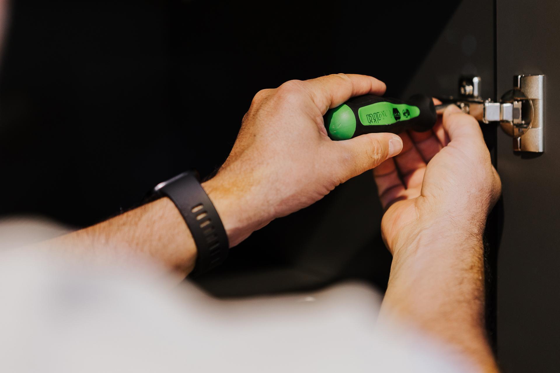 Nahaufnahme eines Seipp-Mitarbeiters bei der Justierung eines Scharniers mit grünem Schraubendreher in einer Küche.