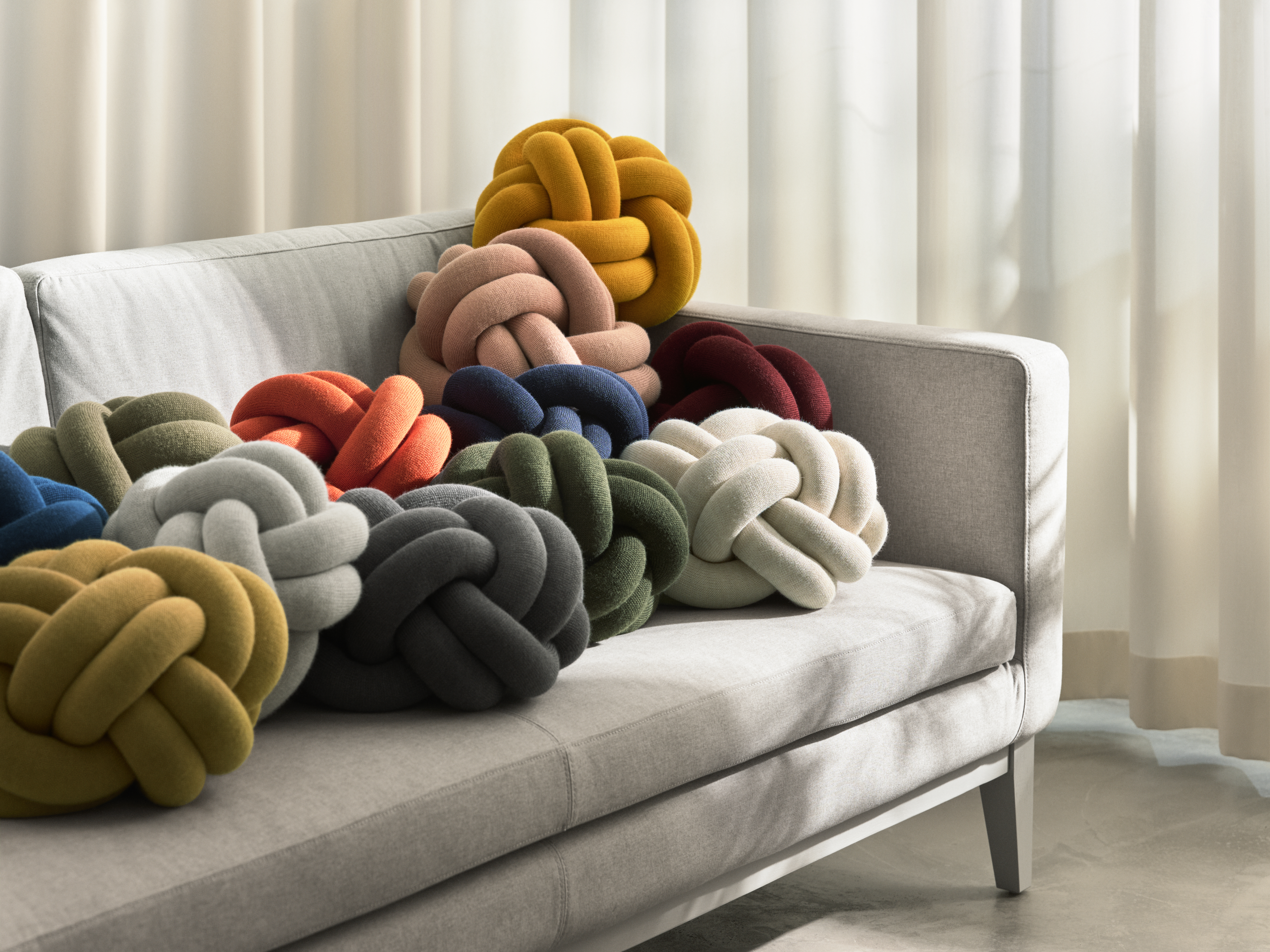 Mehrere Knot-Kissen von Design House Stockholm in verschiedenen Farben auf einem Sofa arrangiert