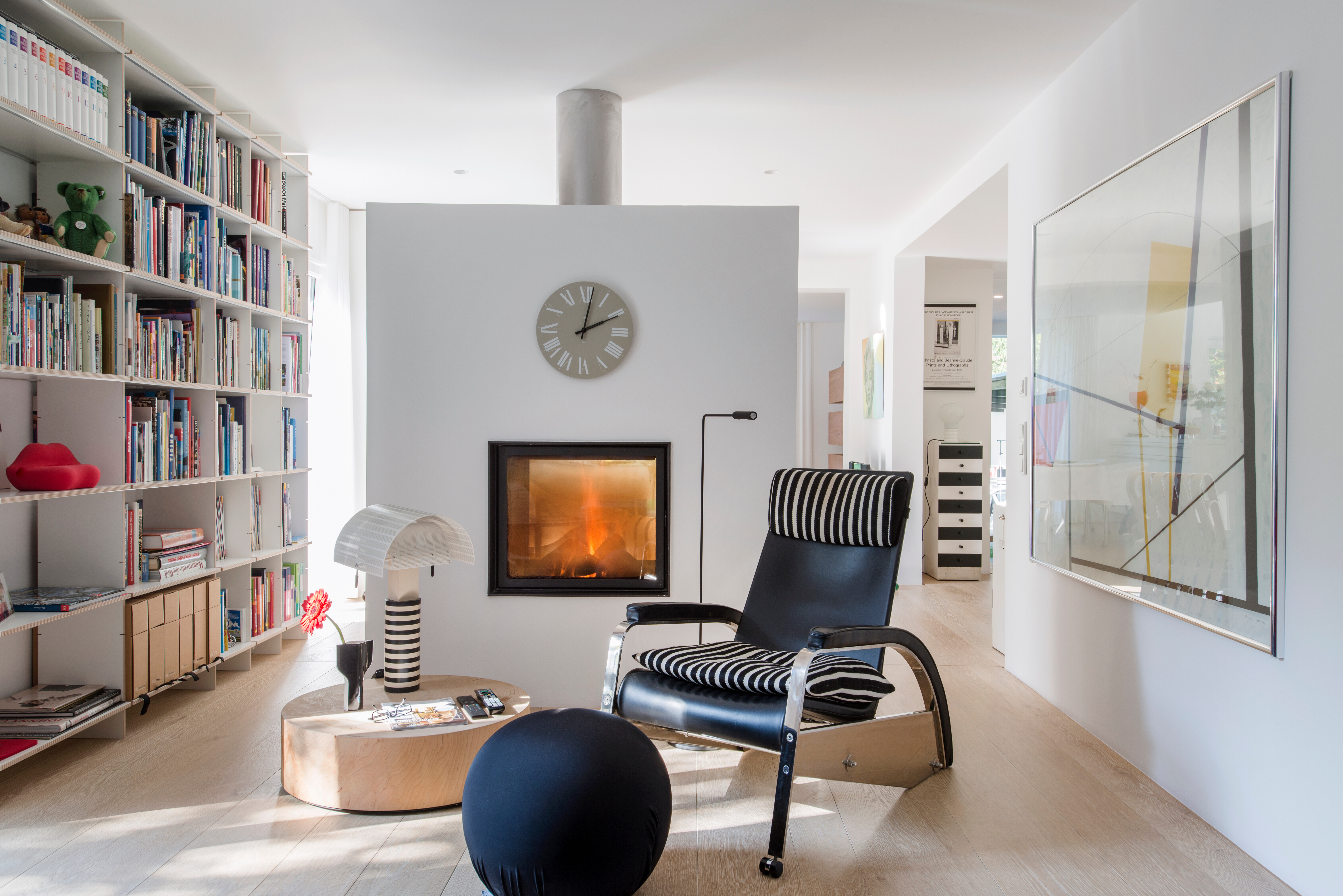 Lesebereich mit Kamin, schwarzem Loungesessel und Bücherwand in hellem, modernem Wohnambiente