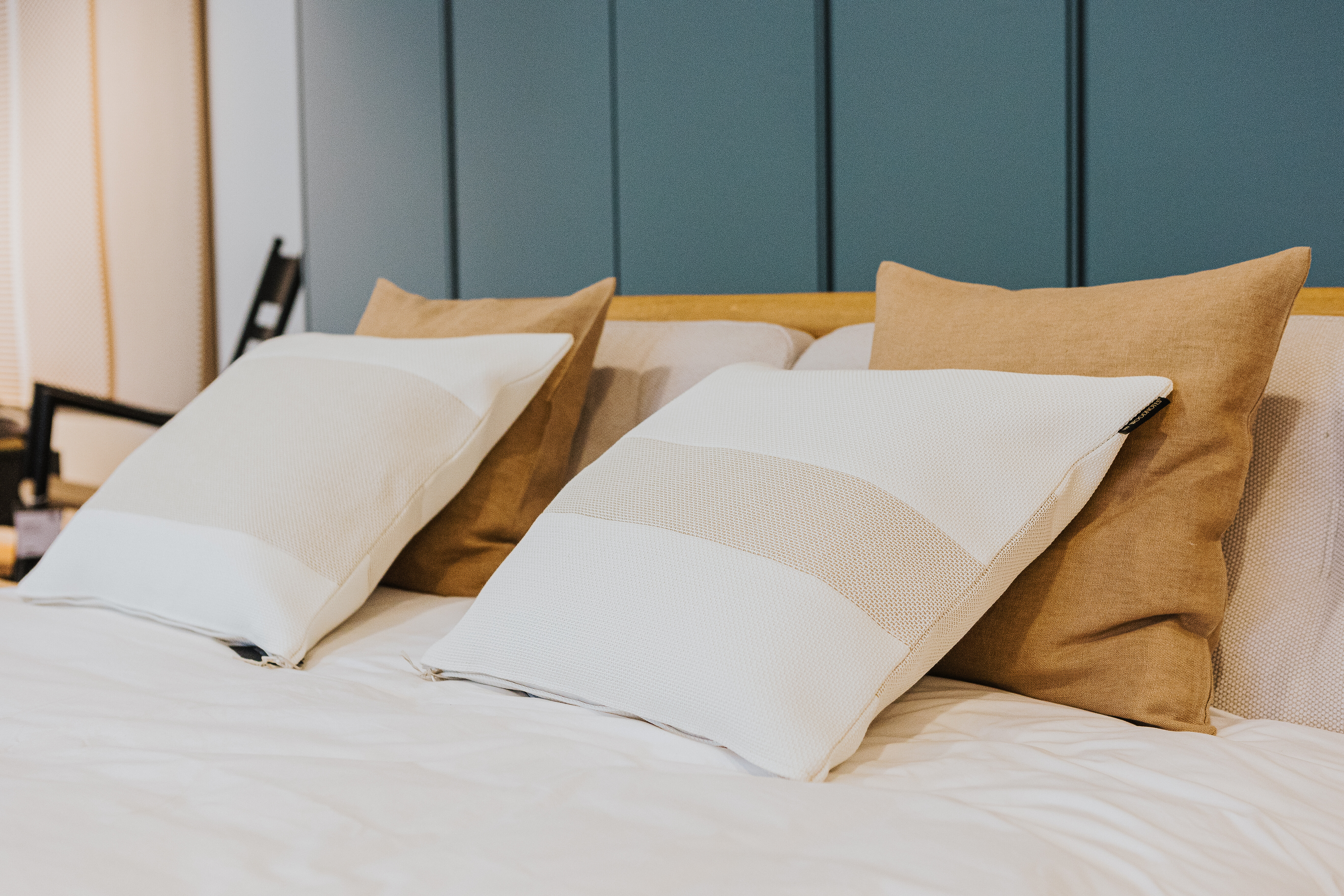 Zwei weiße und zwei sandfarbene Zierkissen auf einem Bett