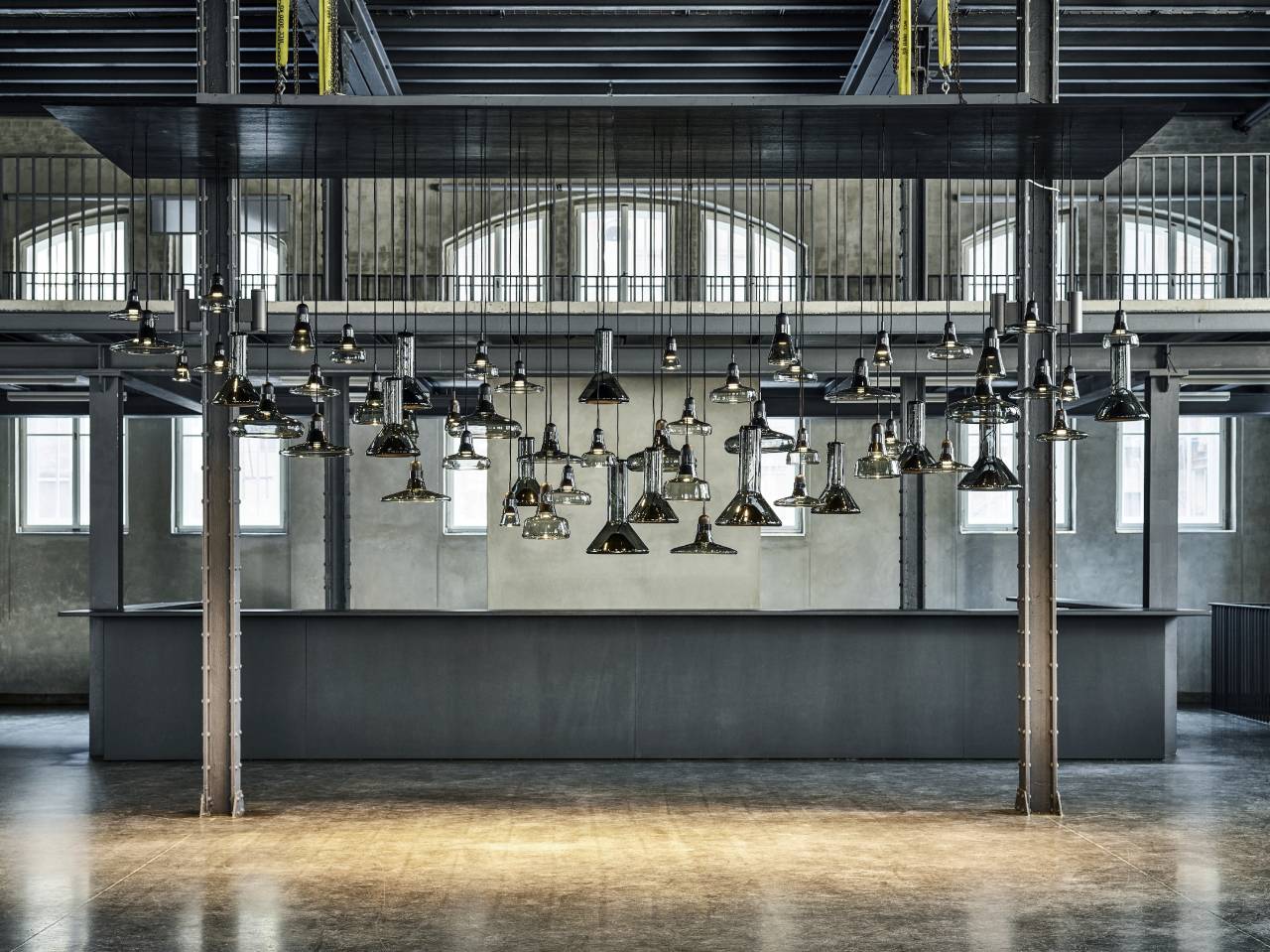 Mehrere Brokis-Leuchten hängen in einer ehemaligen Industriehalle